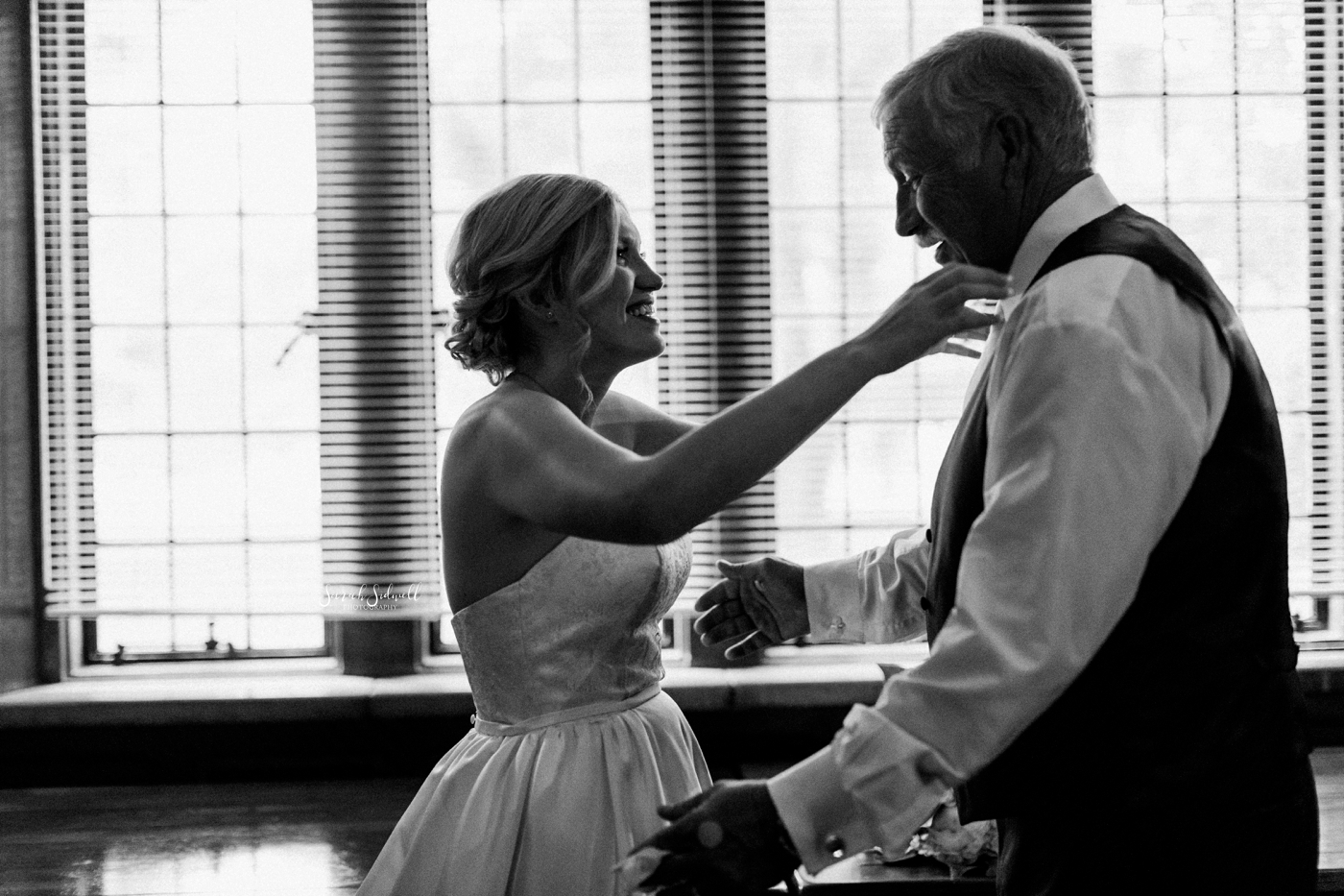 A bride reaches up to hug her father around the neck. 