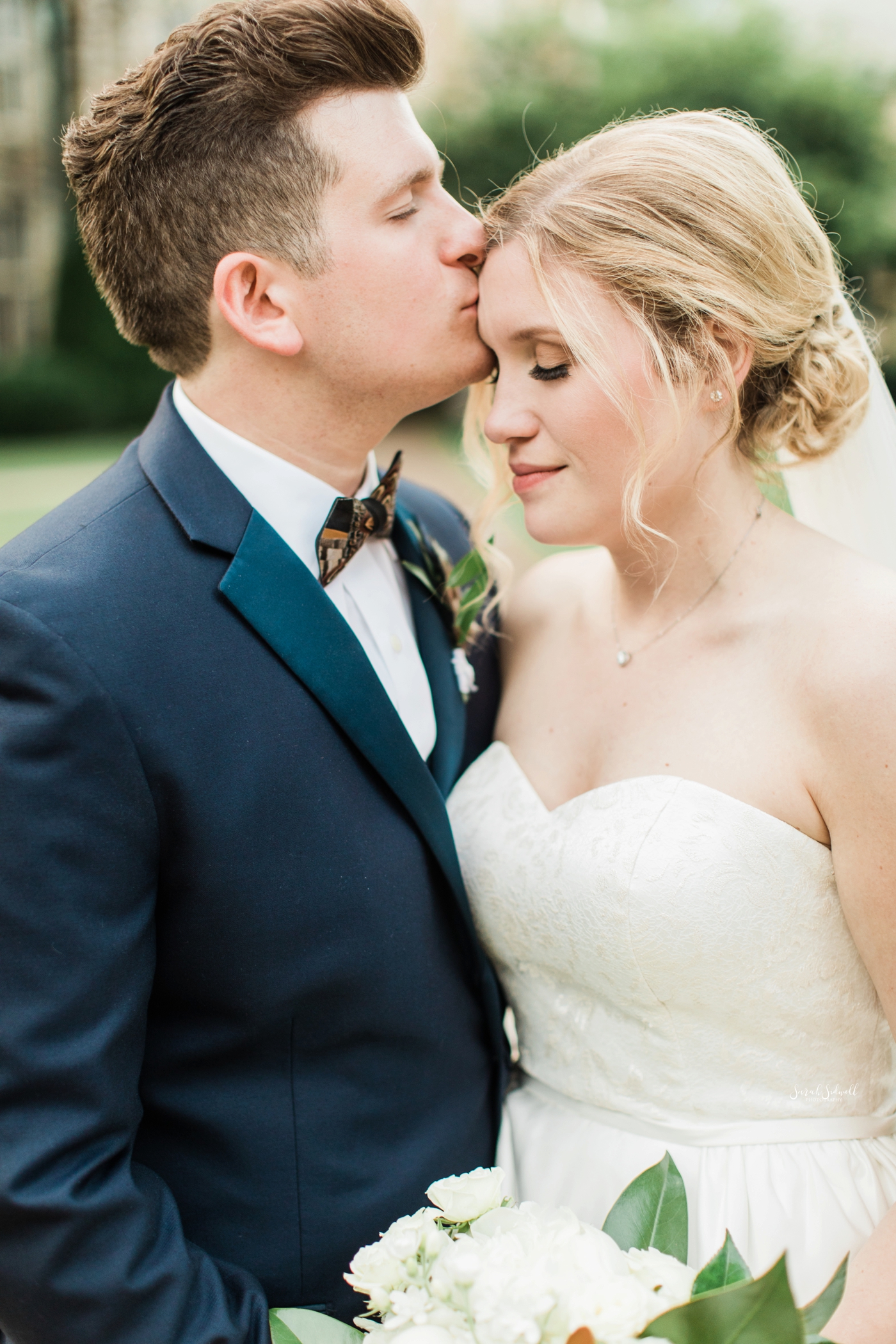 A groom kisses his bride on the forehead. 