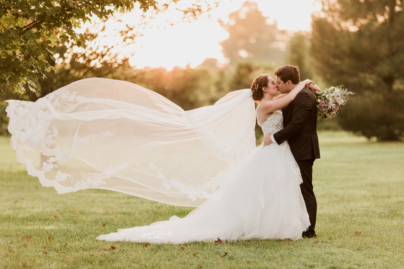 A bride's veil blows in the wind as she kisses her groom. 