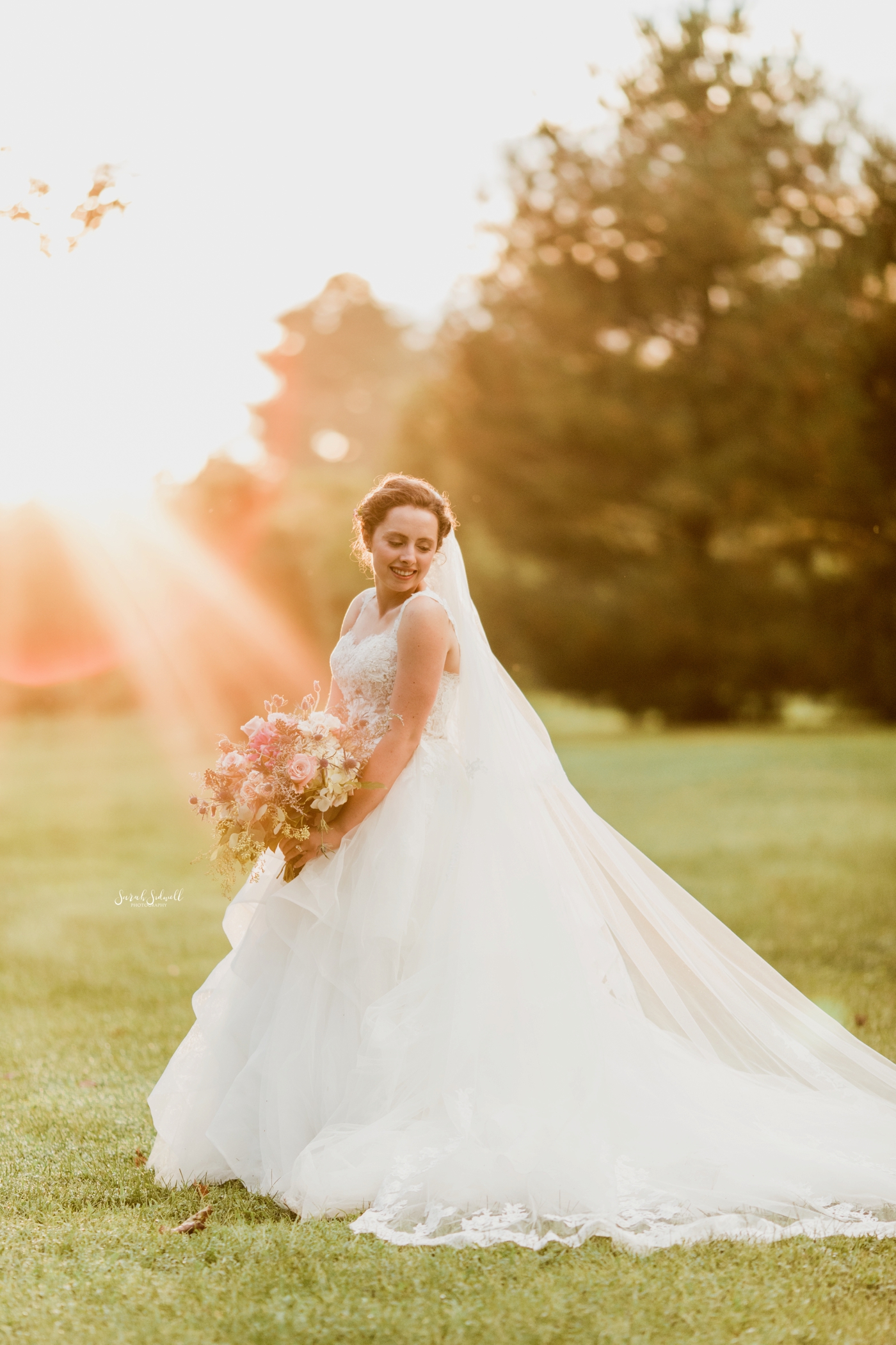 A woman stands in the sun to take a photo in her wedding dress. 