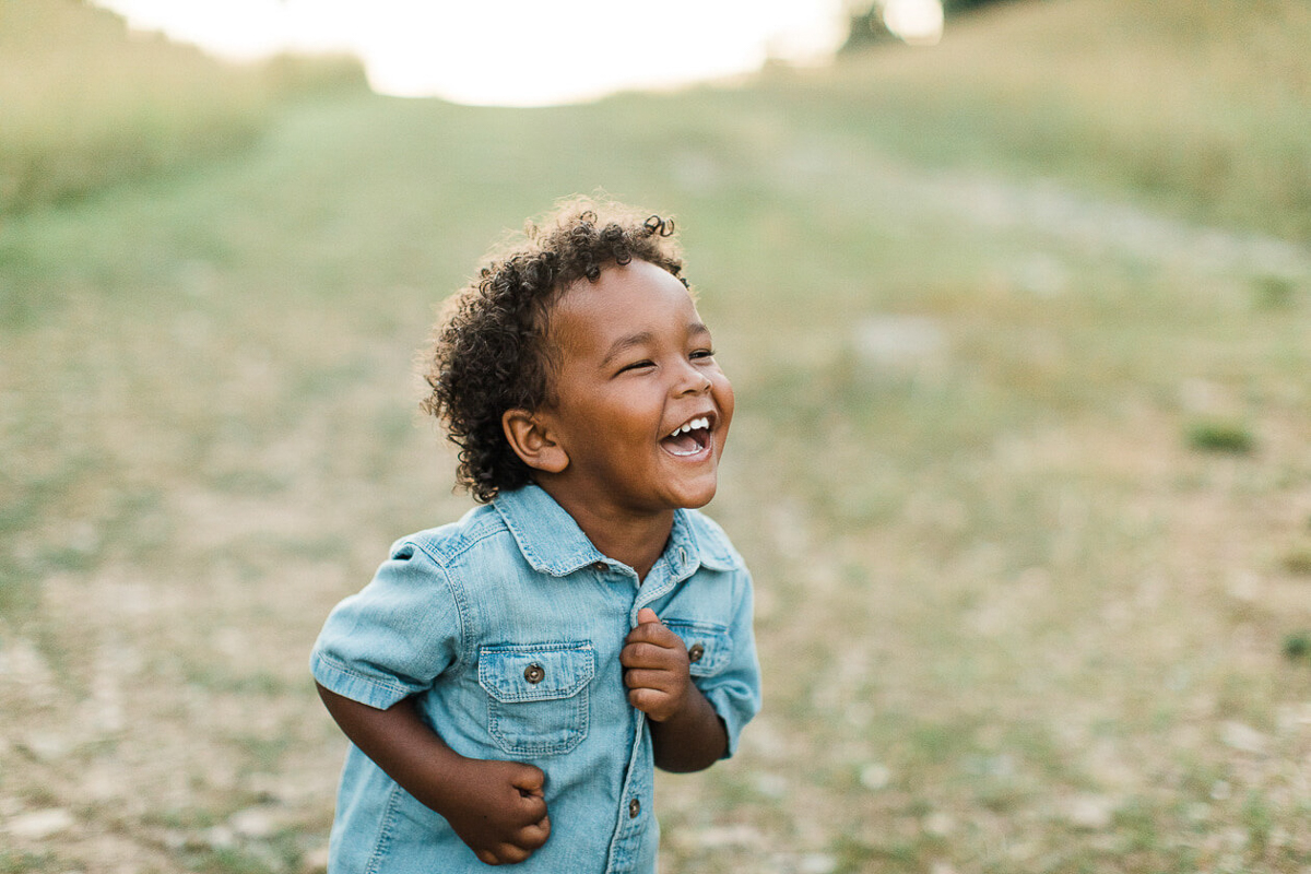 Photo of smiling little boy wearing a jean short sleeve button up. Little boy photographed outdoors by Nashville children photographer.
