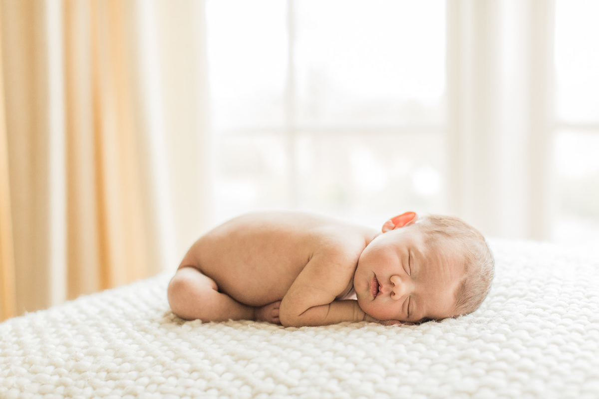 Photo of naked newborn baby boy bundled up in fetal position while laying on belly on white blanket. Photographed by Nashville newborn photographer Sarah Sidwell.