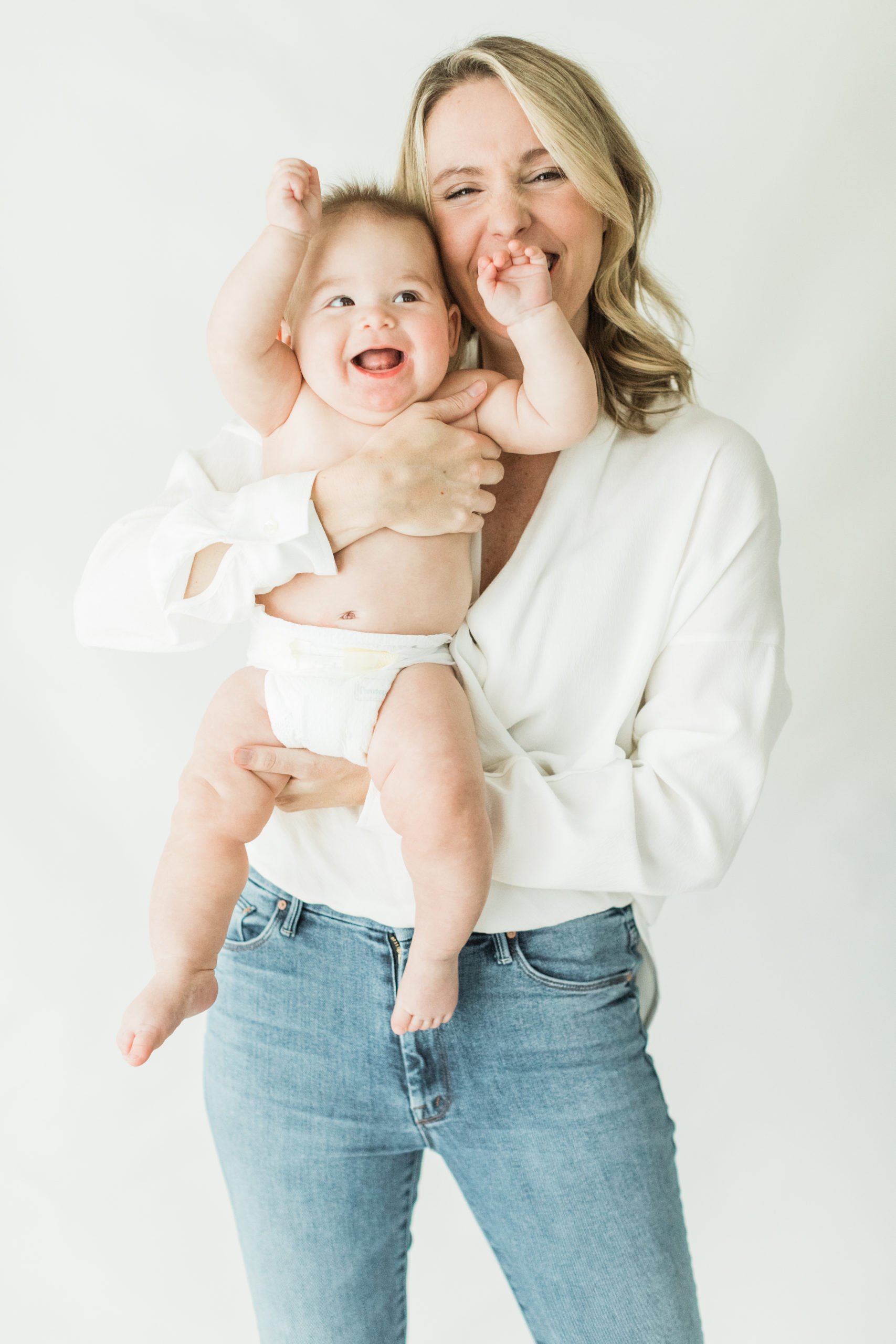 Mom holding her 6 month old baby boy. Baby boy in diaper, smiling. Mama in white long sleeve shirt and blue jeans. Natural light photographer.