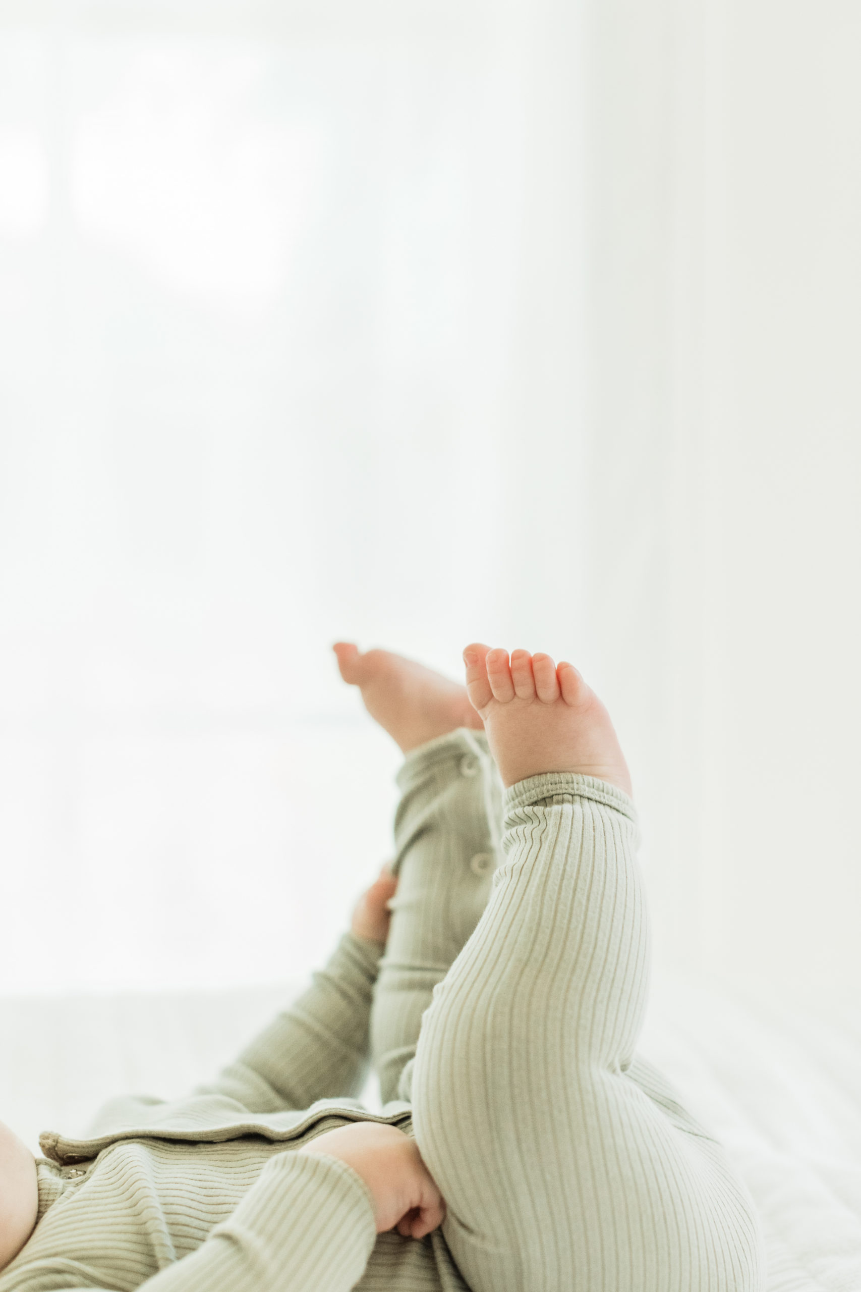 six month old baby boy putting his feet up in the air and wearing light green onesie