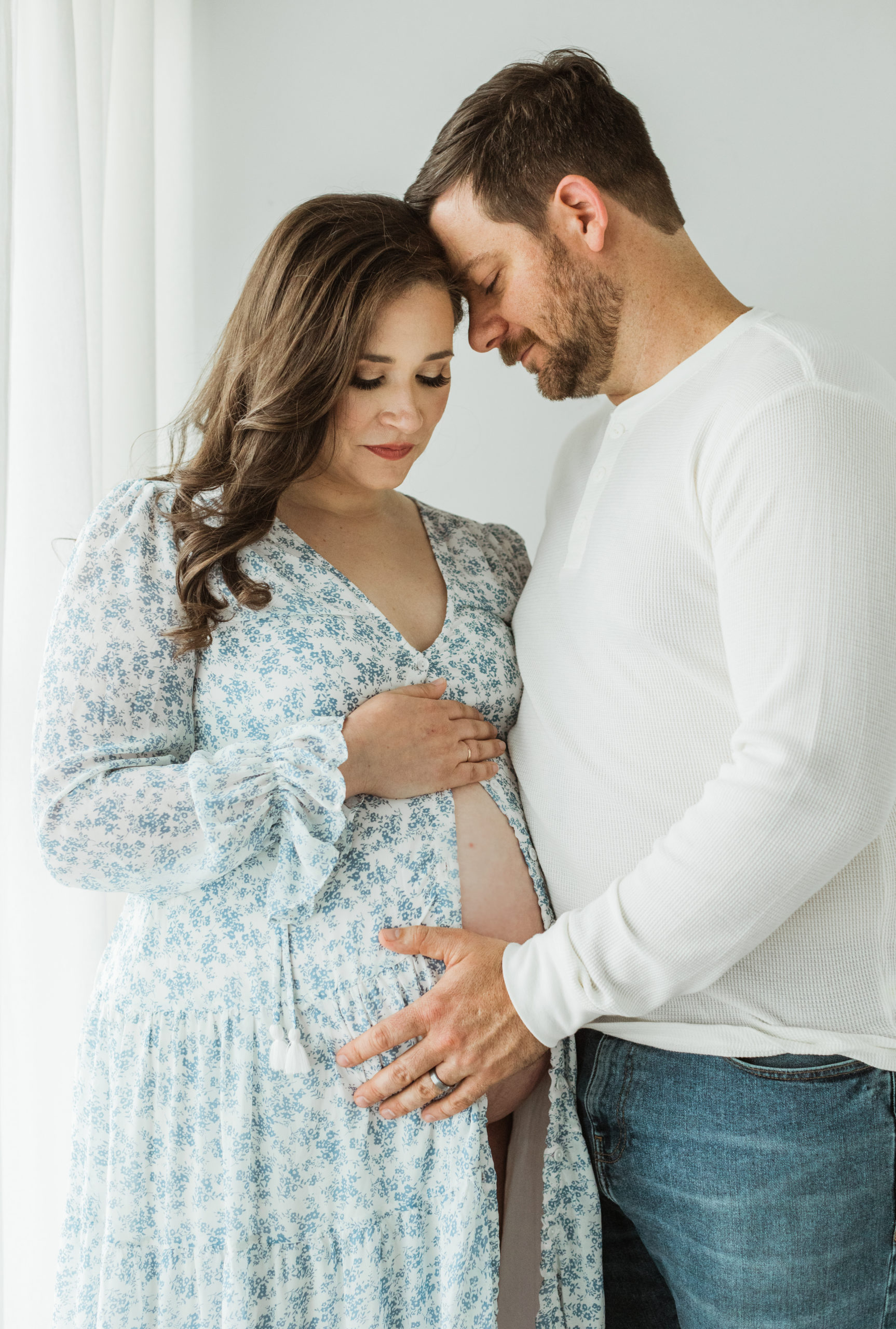 Husband and expecting wife. First time mama wearing white and blue floral cover up. Man wearing white long sleeve and jeans.