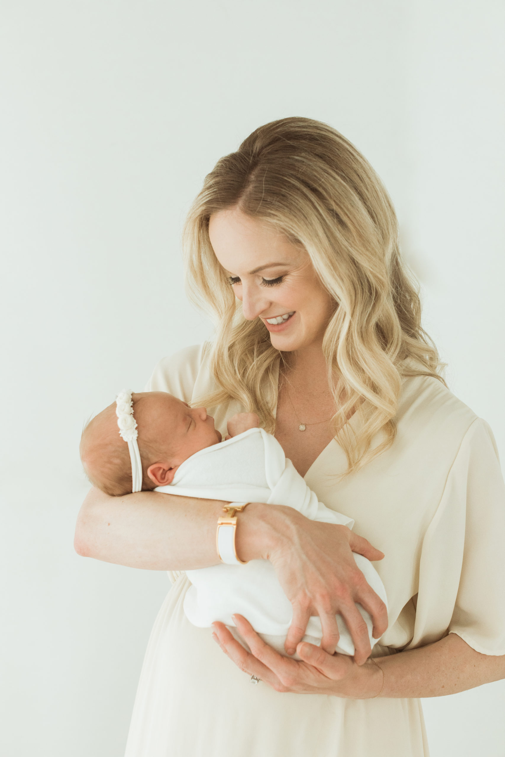 photo of mama holding her newborn baby near her chest. Mama with hair and makeup done by professional HMUA. Mama in creak maxi dress.