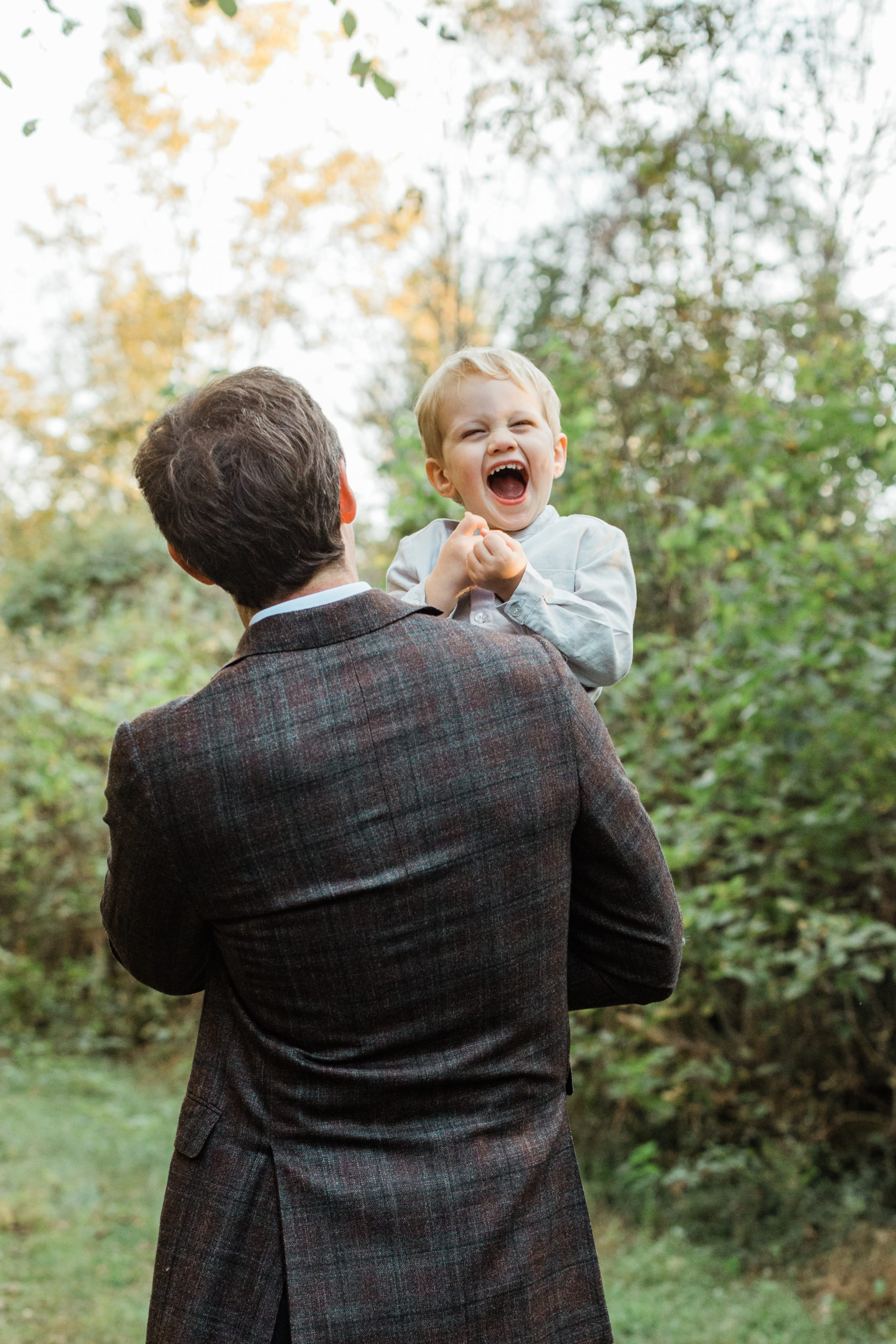 dad's back facing the camera, wearing plaid blazer. dad carrying smiling son over his shoulders.