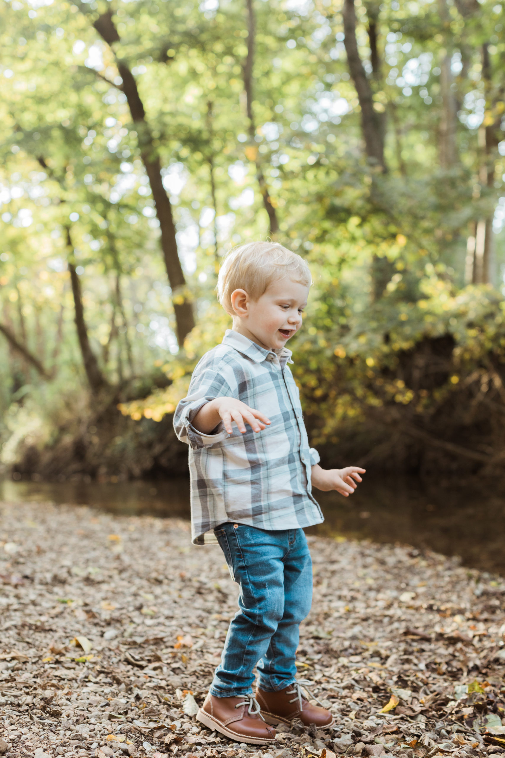 Little boy outdoors looking at fall leaves. Boy wearing jeans and plaid button up.