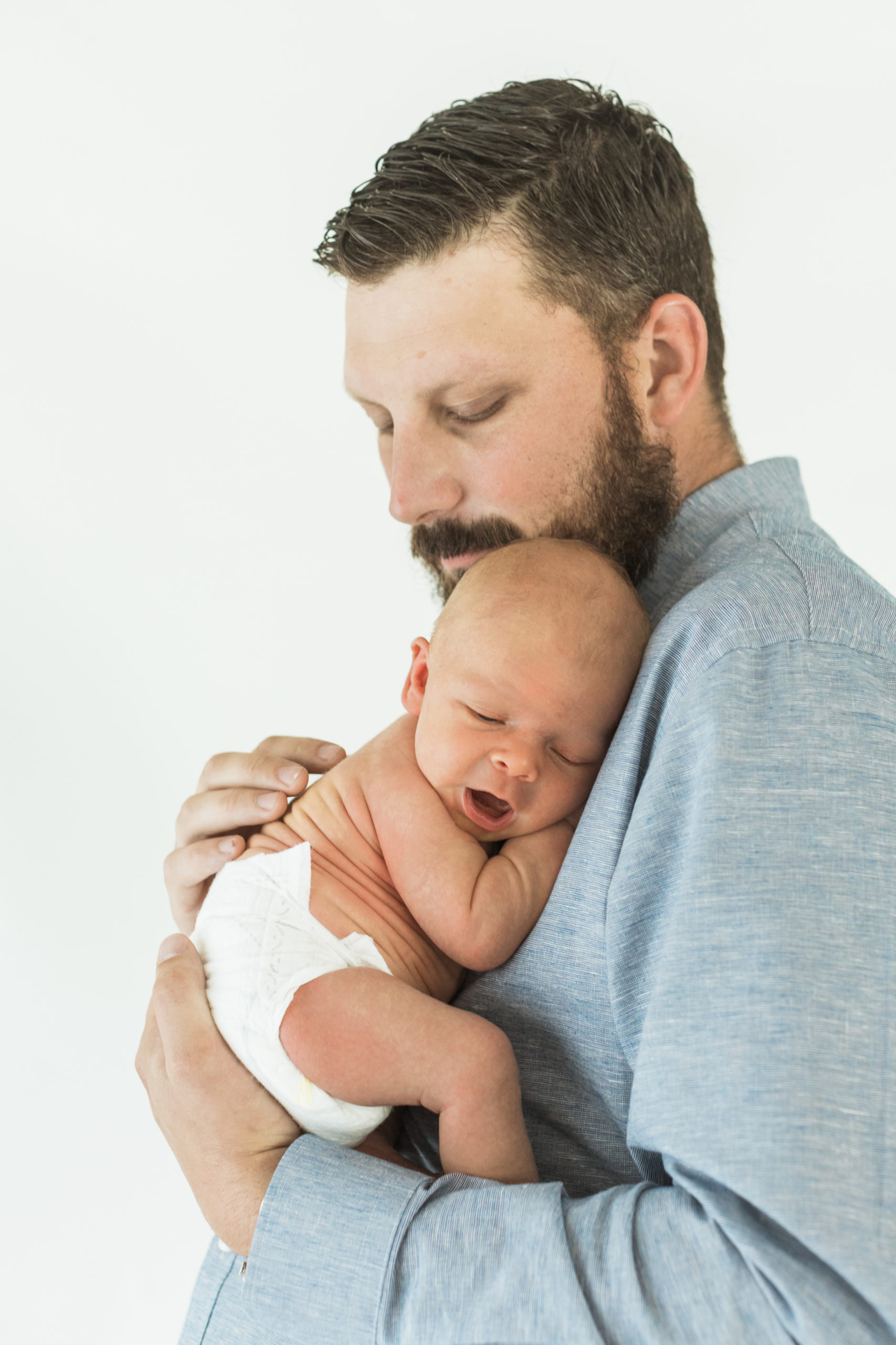 photo of dad holding his newborn son to his chest. Dad wearing light blue button up.