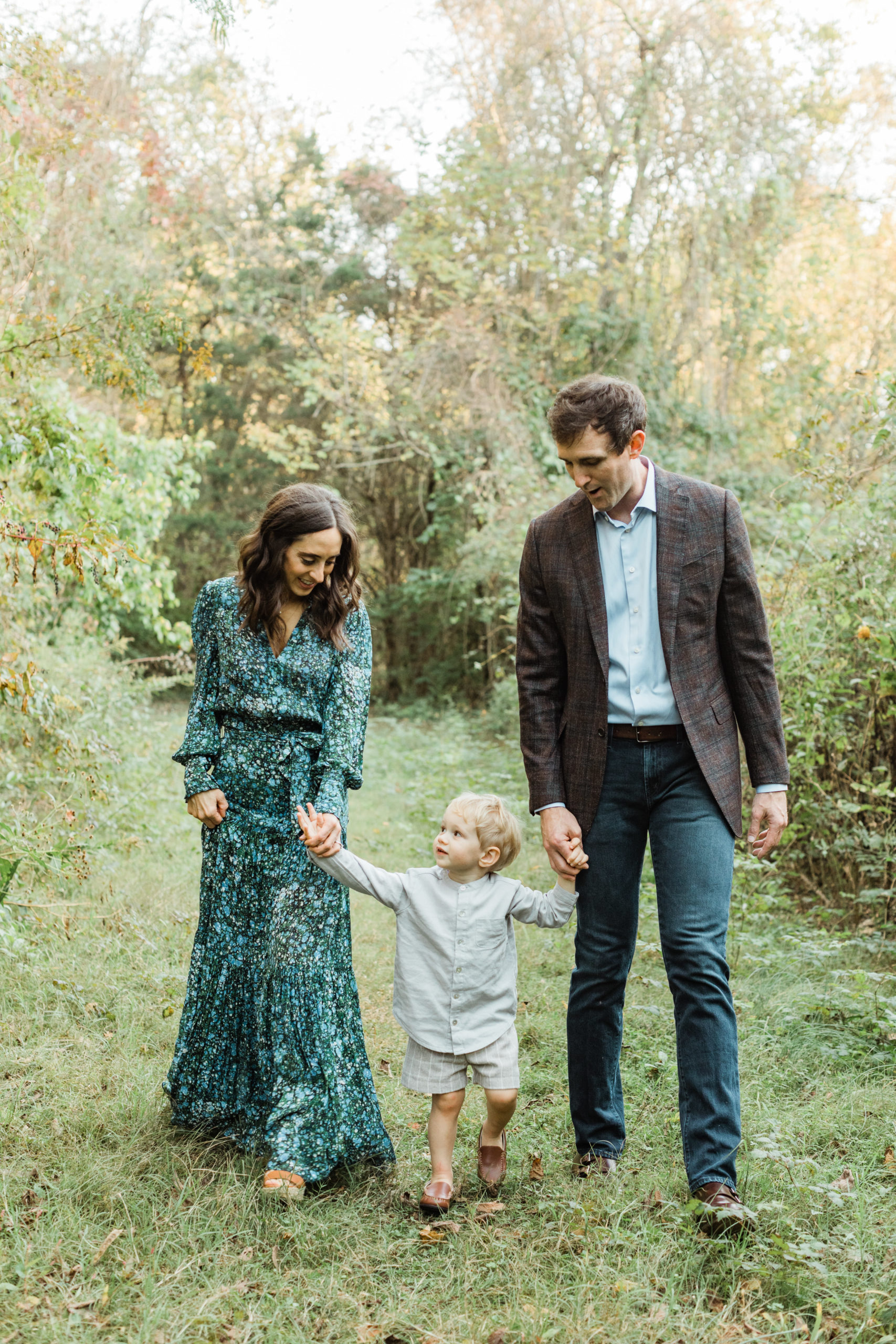 family of three. mama in long sleeve maxi dress, turquoise blue printed dress. little boy in plaid grey shorts and light grey button up. dad in jeans and light blue button up and brown plaid blazer.