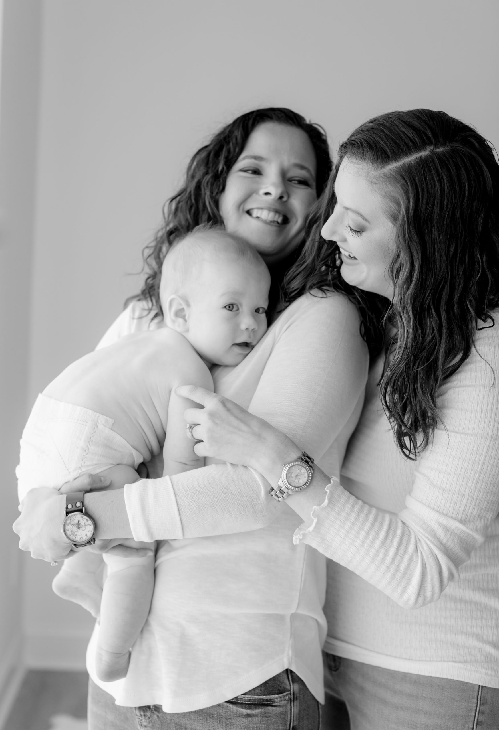 Photo of two mamas and their 6 month old baby boy. LGBTQ. Mamas wearing white long sleeves and blue jeans.