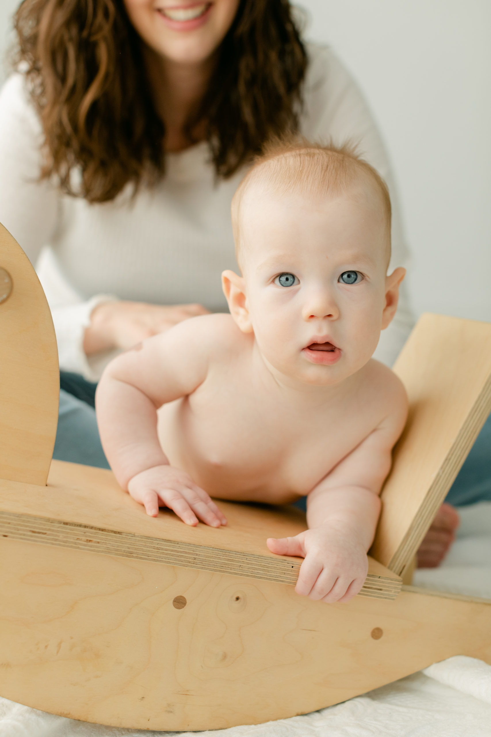 6 month old baby boy with blue eyes leaning on wooden rocking horse.
