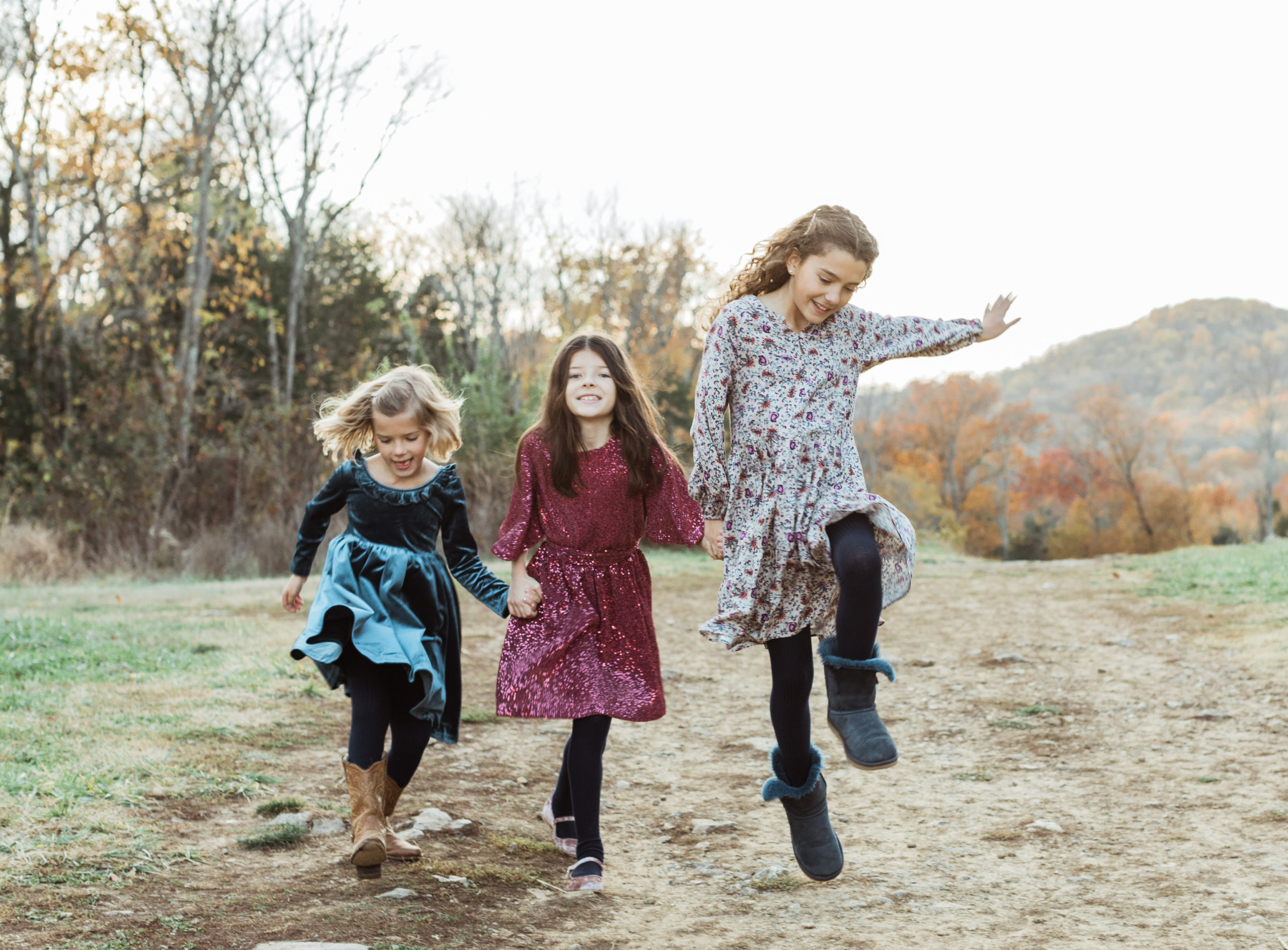 Three young sisters holding hands and skipping jumping around. Fall family photos.