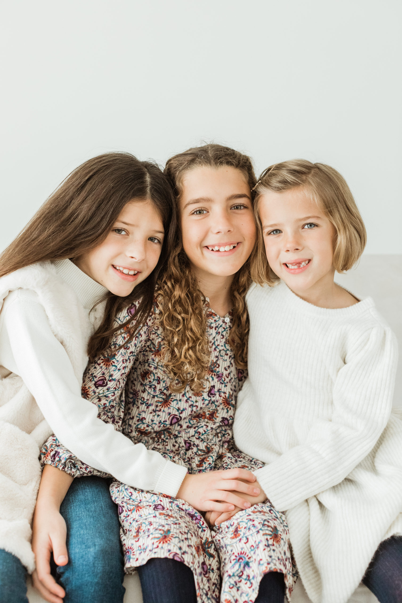 Photo of three young sisters sitting closely hugging and smiling.