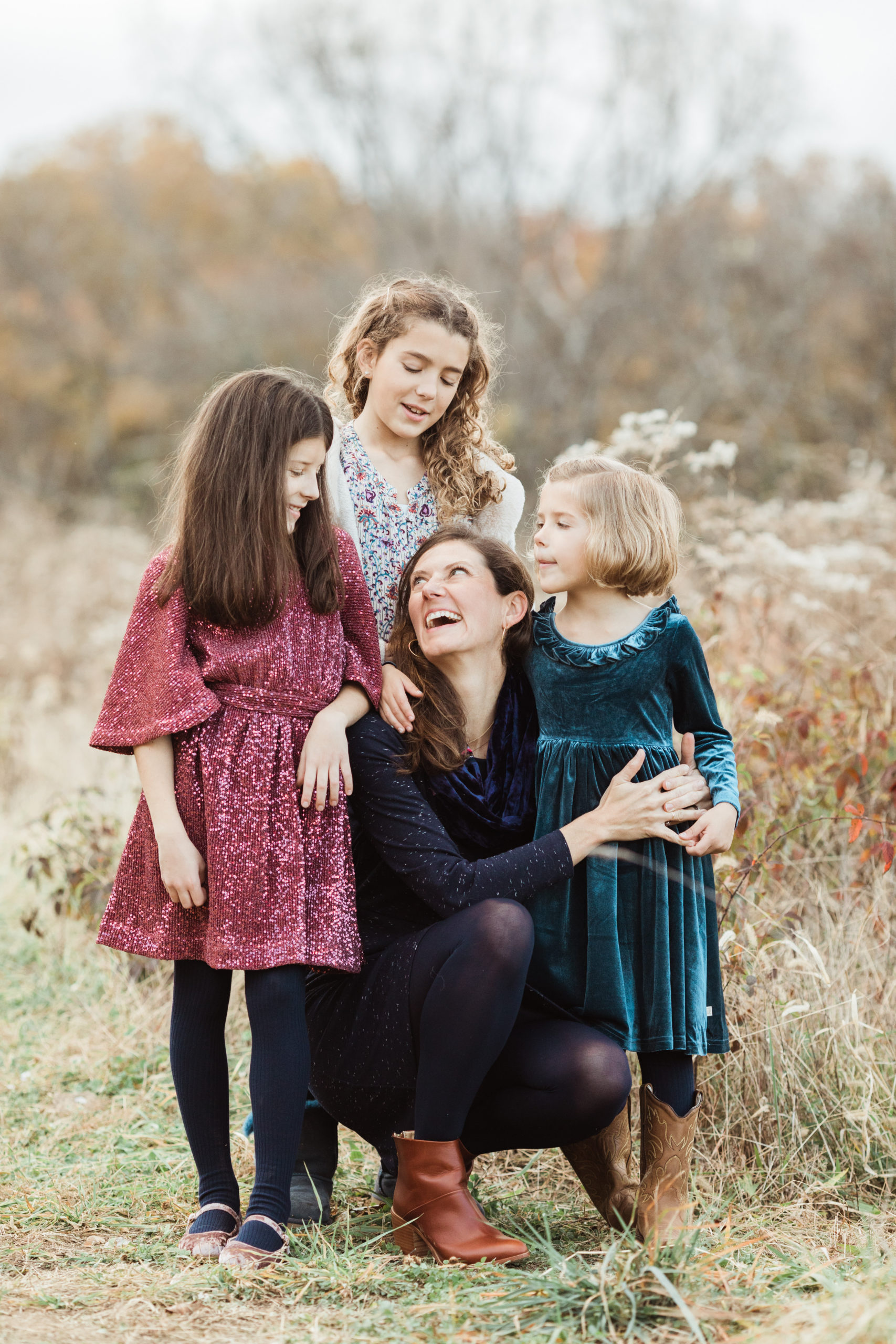 Mom squatting and hugging her daughters. Outdoor fall family photos.