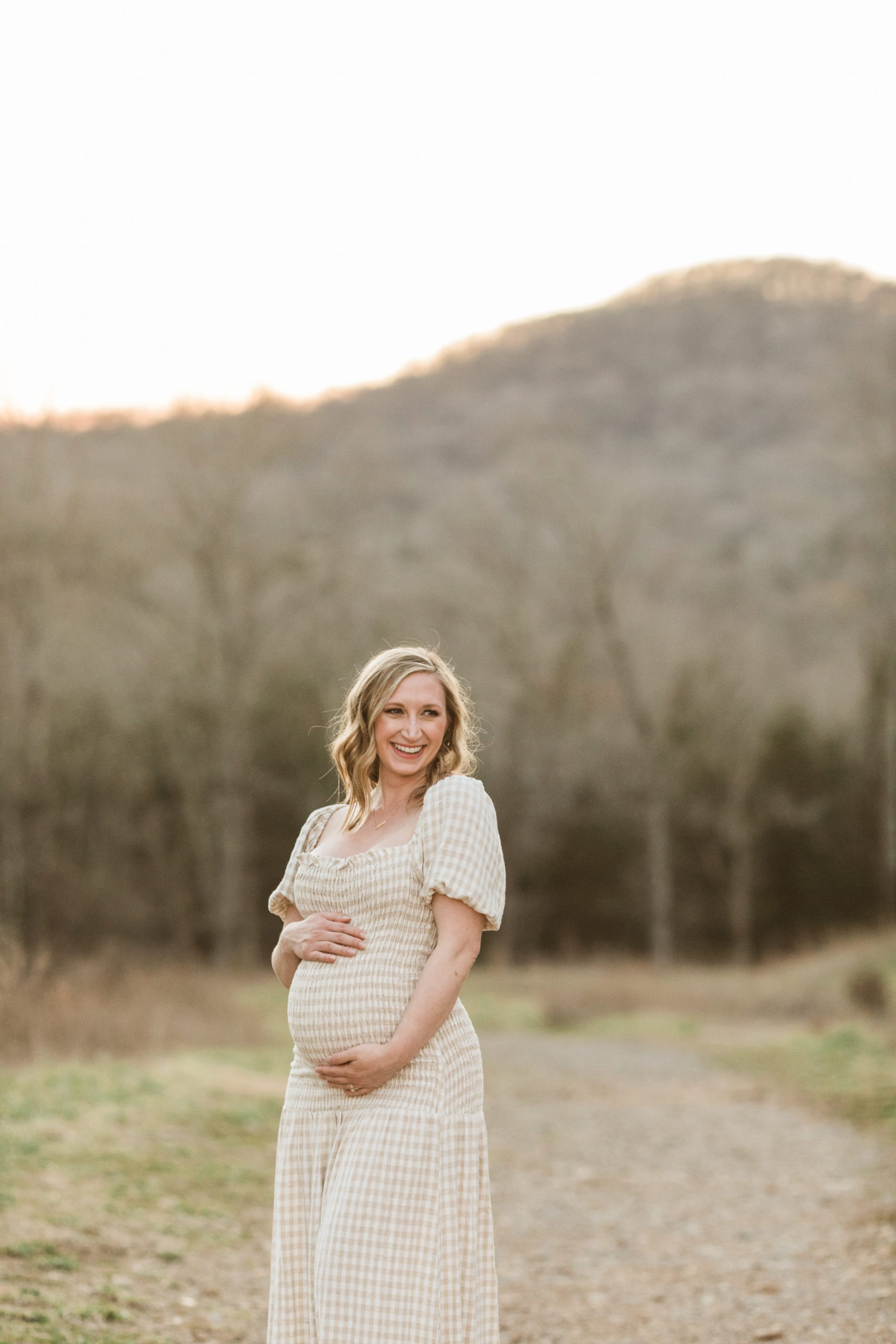 gigham cream and white midi dress showing off pregnant belly. outdoor maternity session.