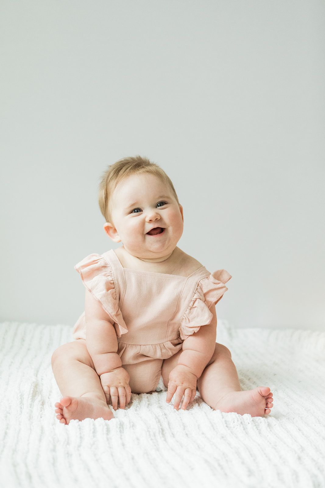 photo of 7 month old baby girl. she's sitting down and smiling big