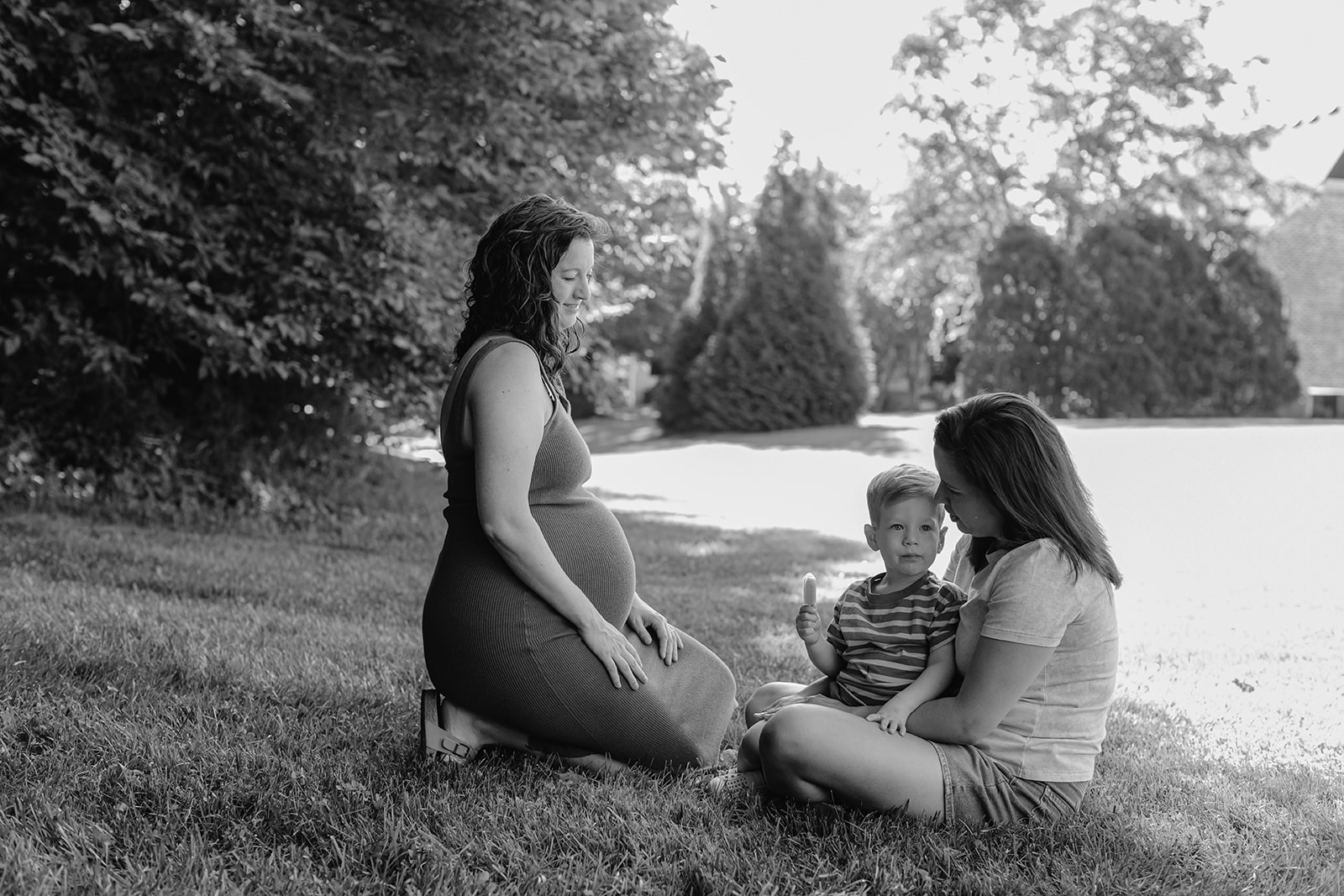 Moms sitting with son during backyard summer family session in Nashville, TN