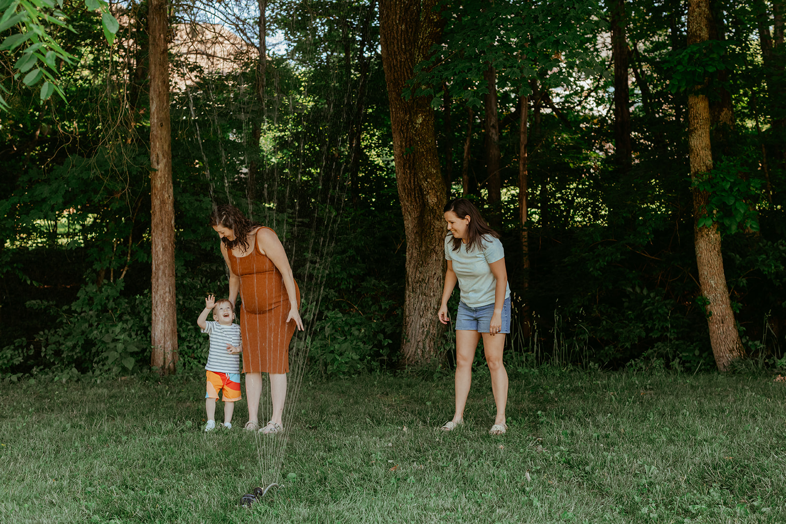 Moms running through sprinklers with son. Backyard summer family session in Nashville, TN