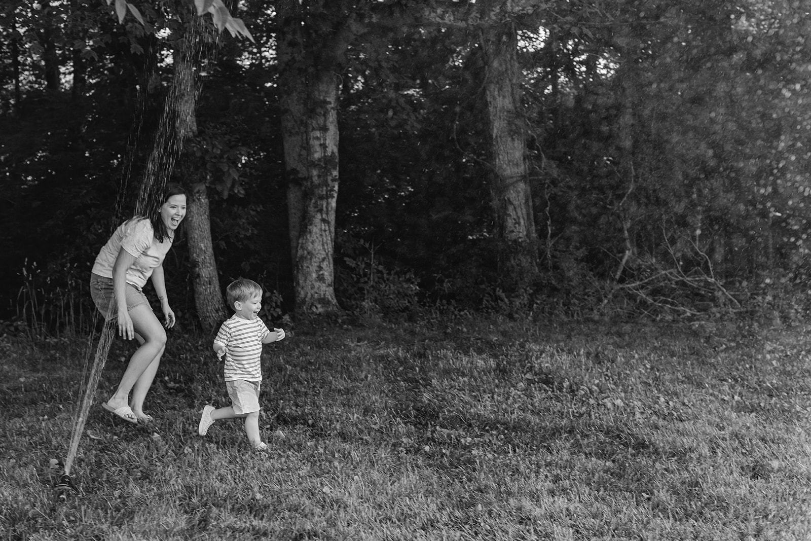 Mom running through sprinklers with son. Backyard summer family session in Nashville, TN