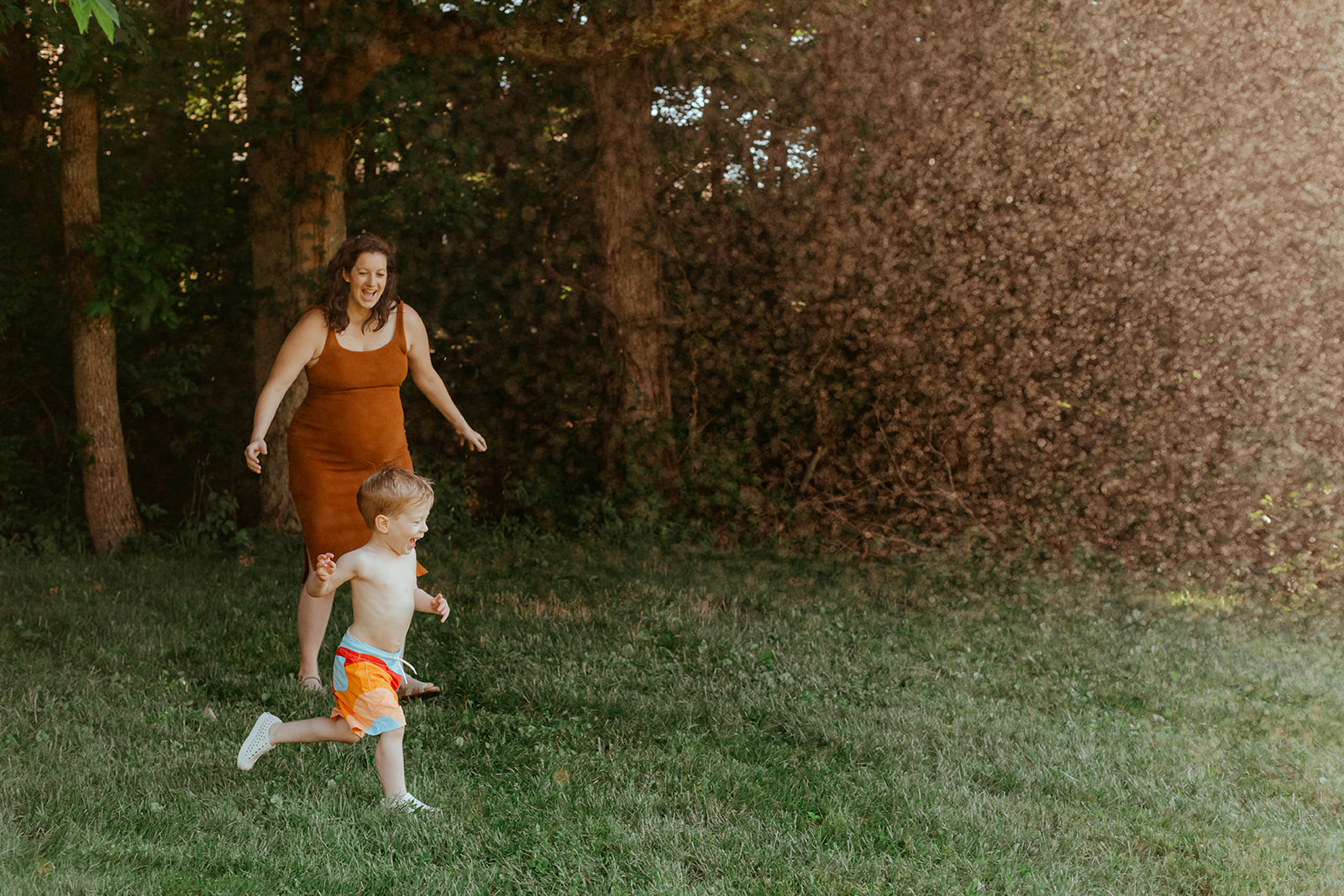 Mom running through sprinklers with son. Backyard summer family session in Nashville, TN