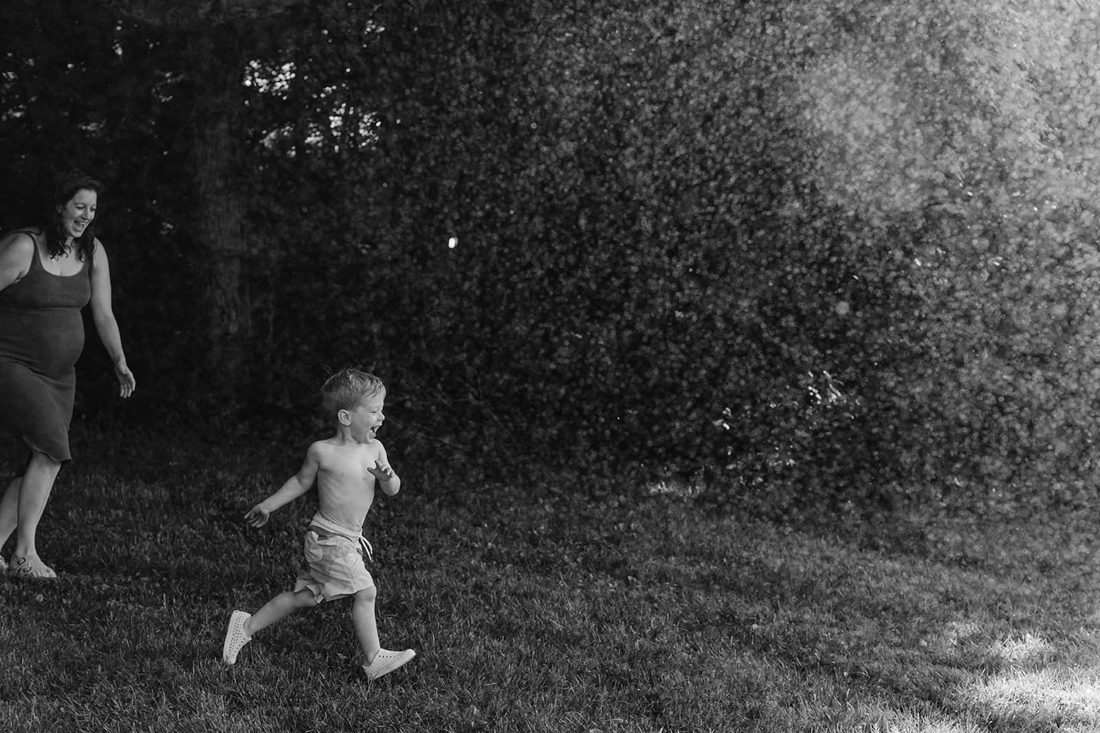 Moms running through sprinklers with son. Backyard summer family session in Nashville, TN