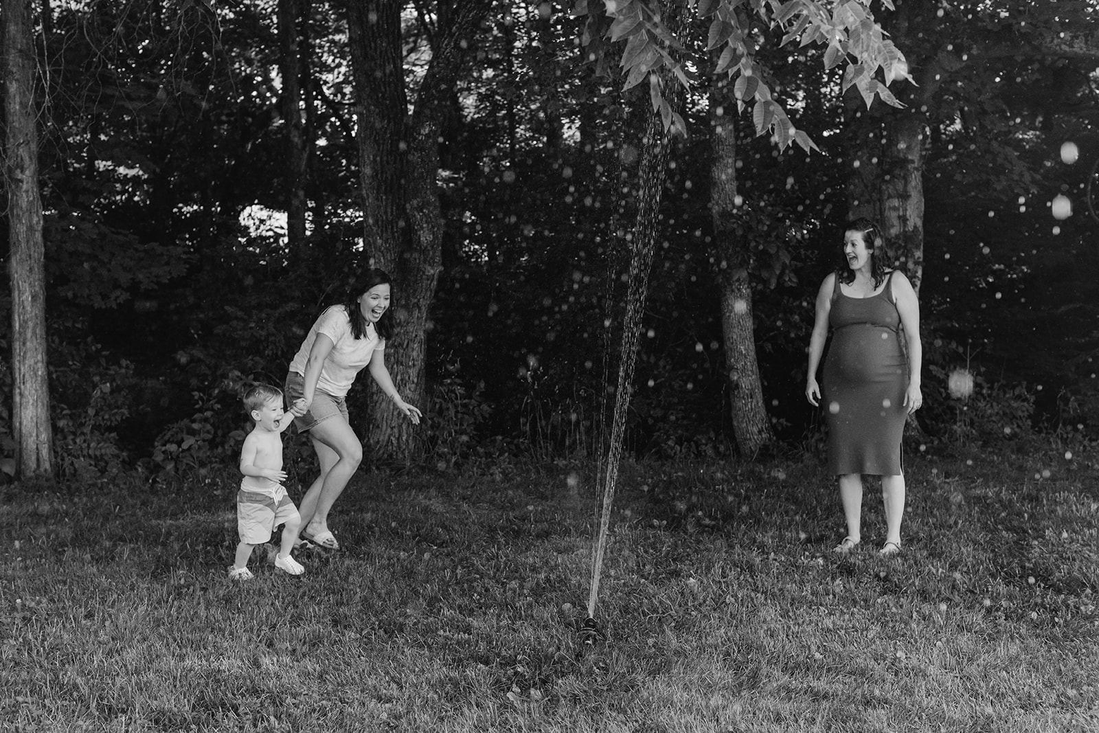 Moms running through sprinklers with son. Backyard summer family session in Nashville, TN