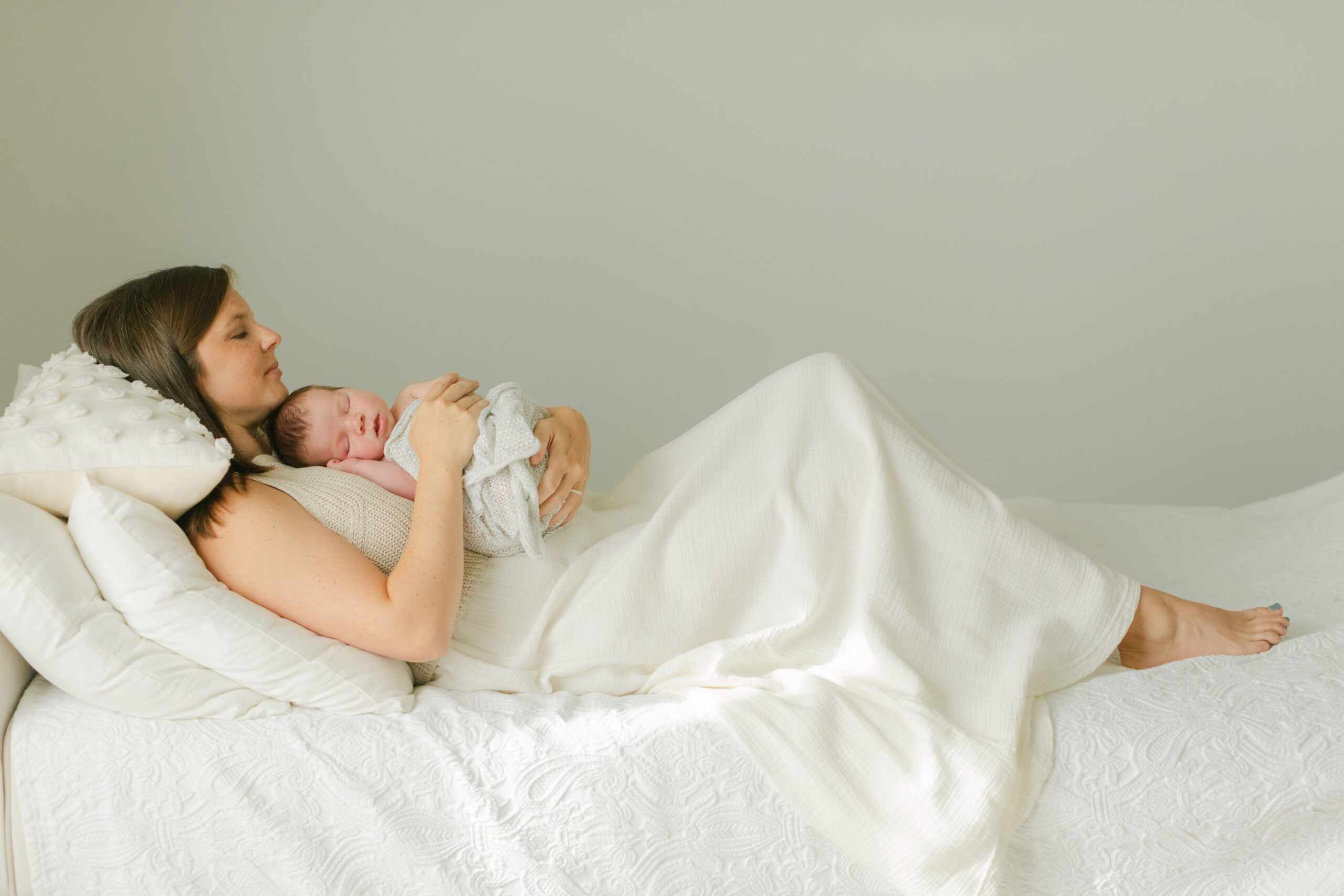 mama laying on sofa bed wearing cream knitted dress holding her newborn baby on chest