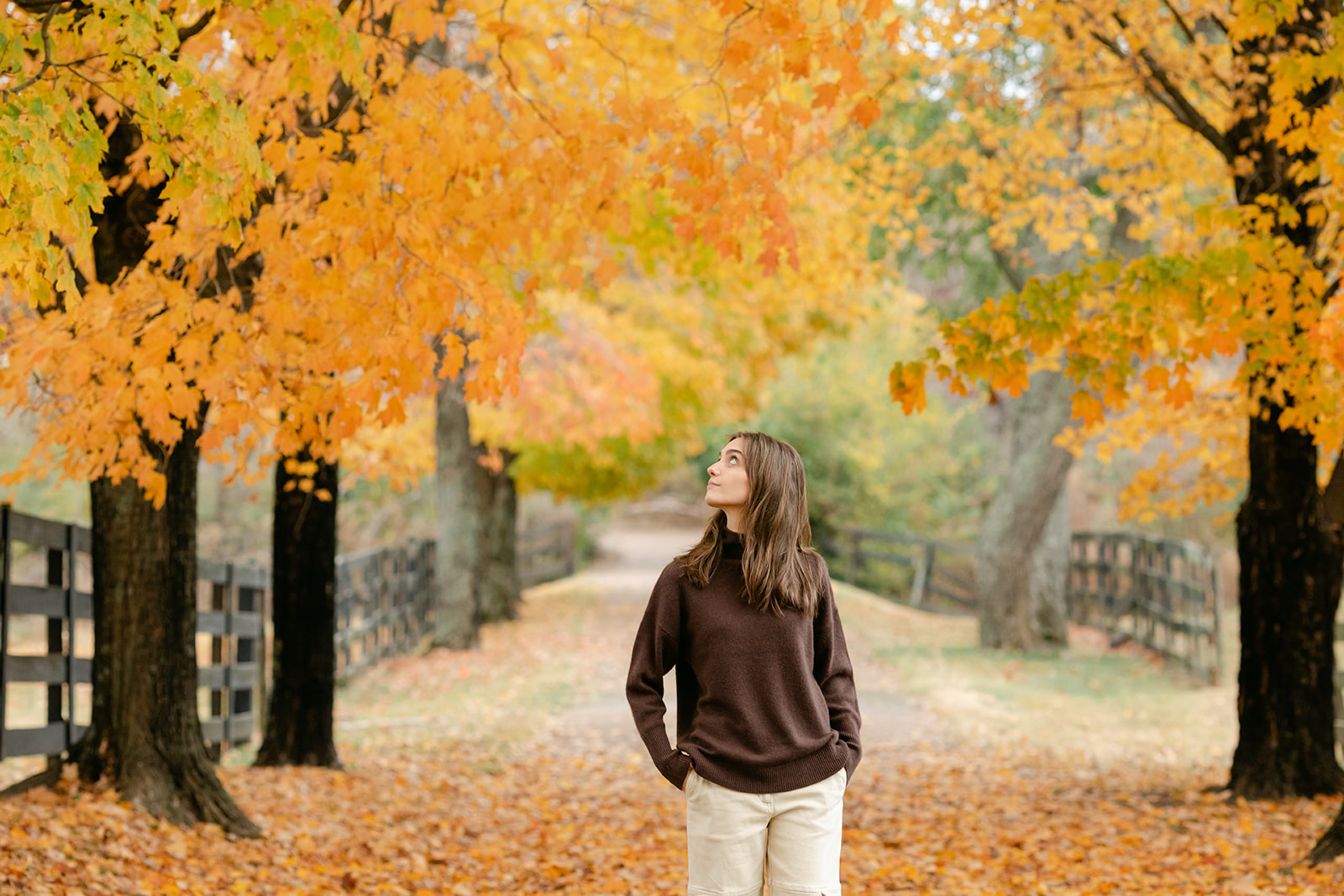 teenage girl during fall senior photos surrounded by fallen fall leaves.