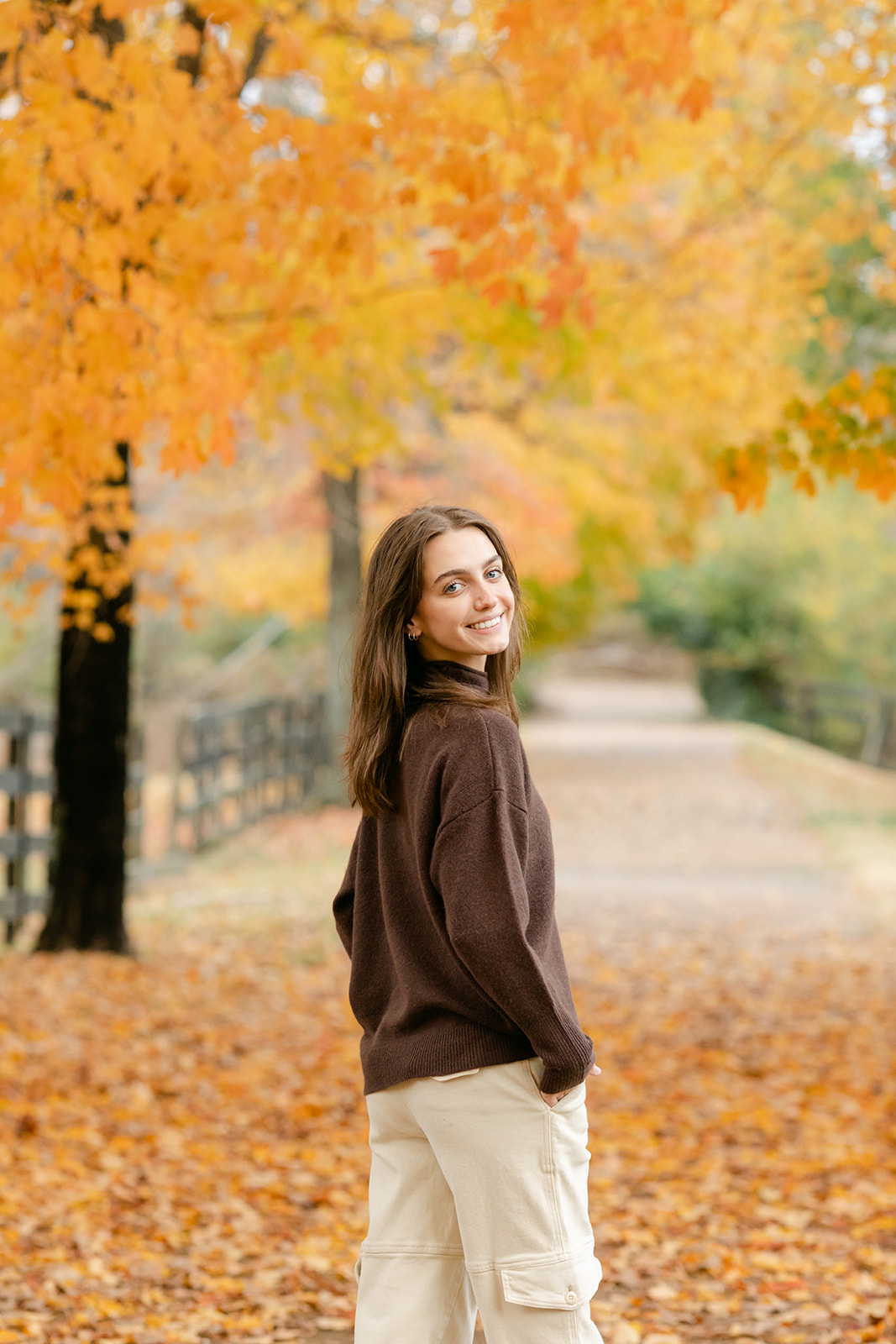 teenage girl during fall senior photos surrounded by fallen fall leaves.