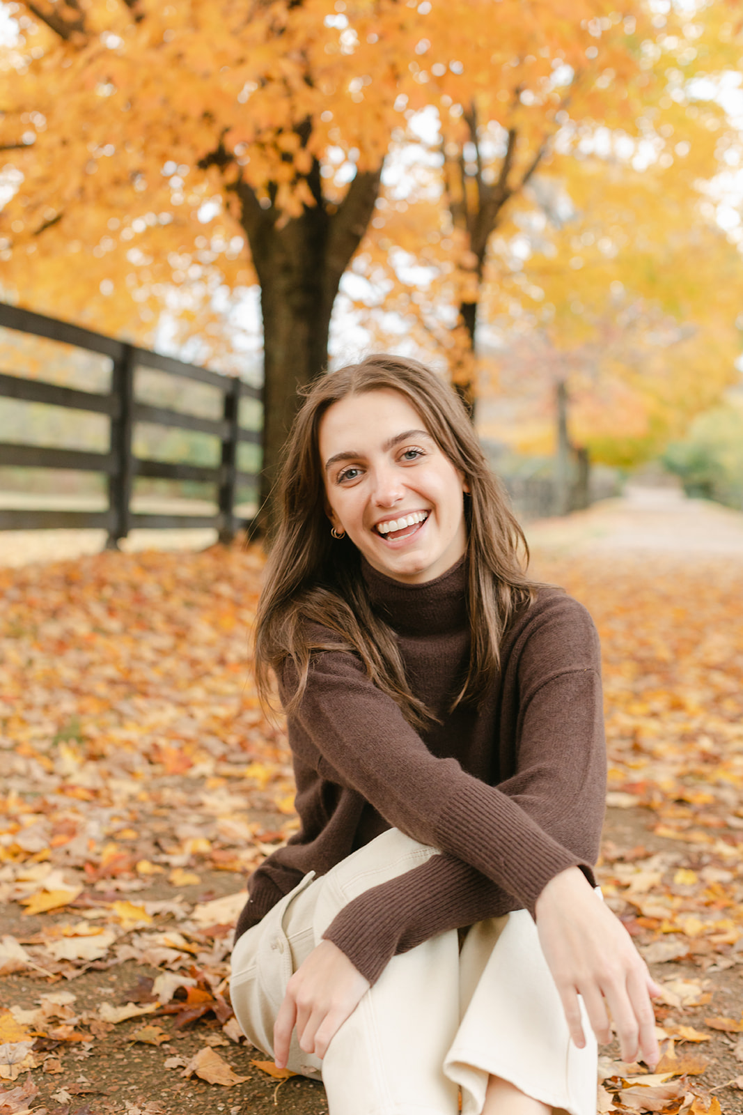 teenage girl during fall senior photos surrounded by fallen fall leaves.