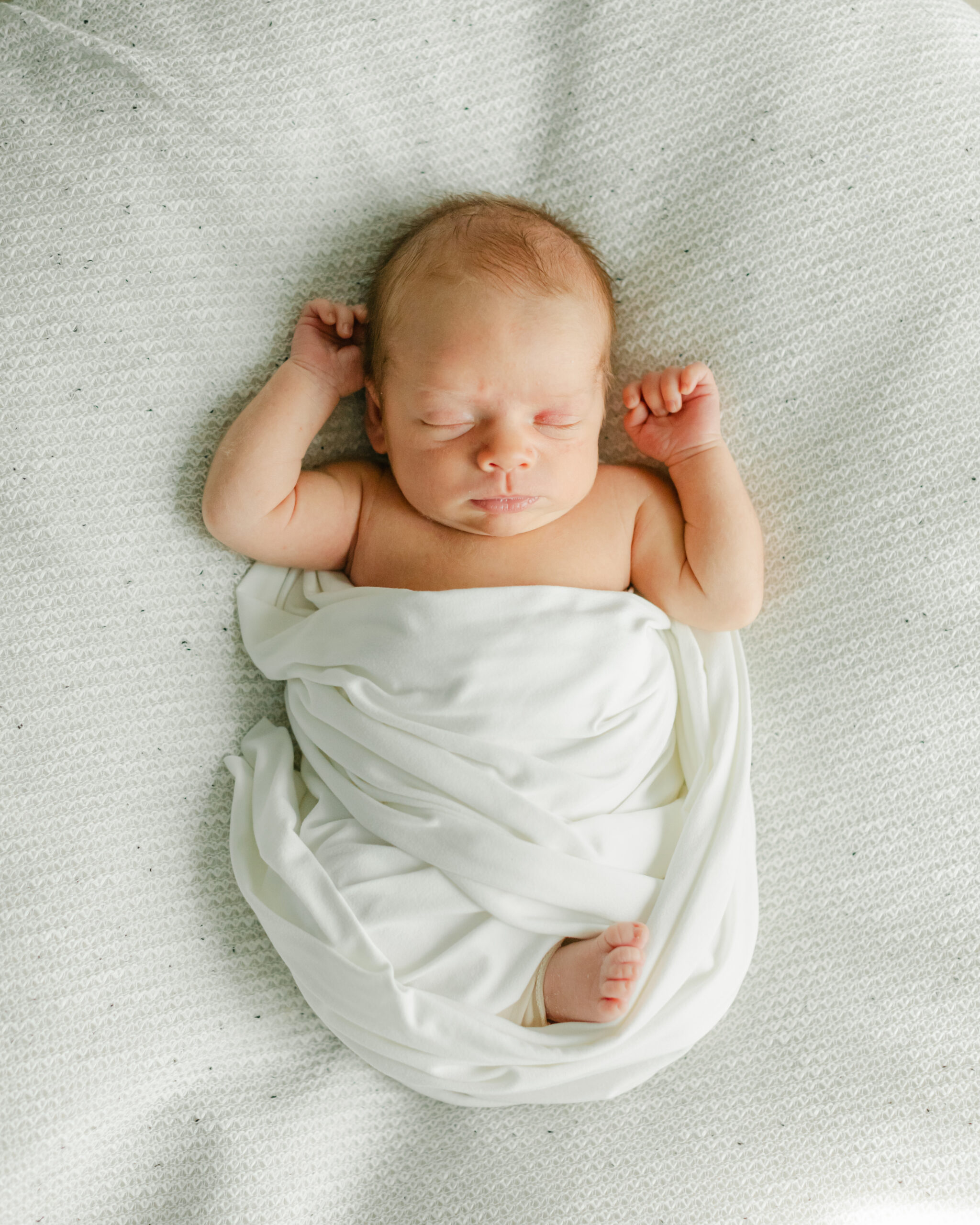 sleepy newborn baby boy in white swaddle