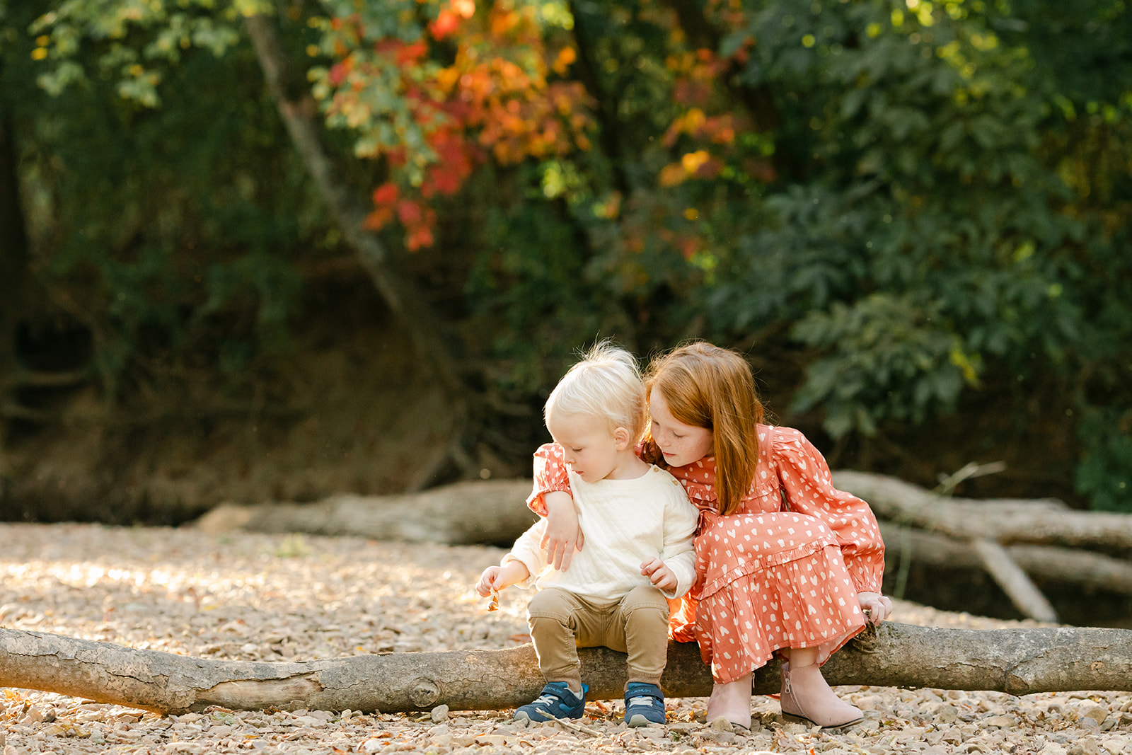 sister and brother sitting by creek during fall family photos at West Nashville Creek