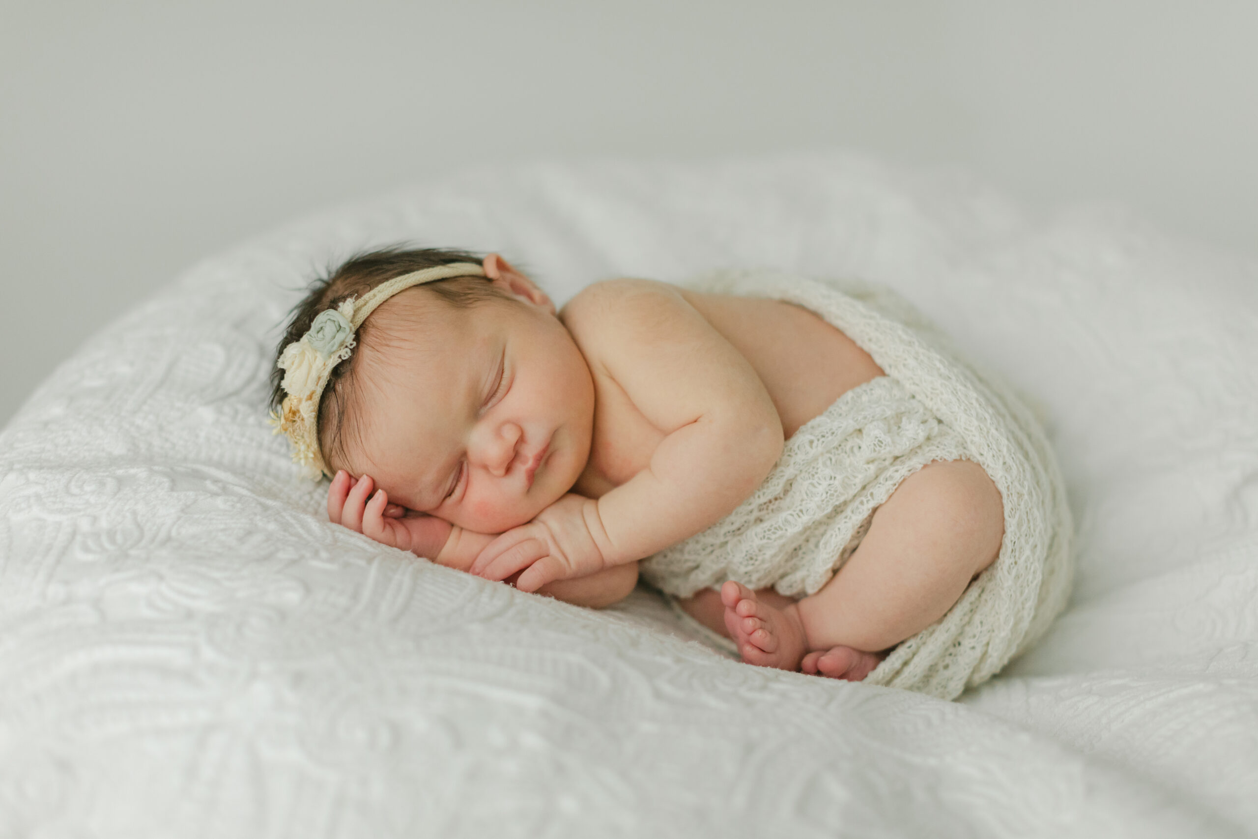 sleepy newborn baby girl wrapped in knit swaddle, wearing knit headband