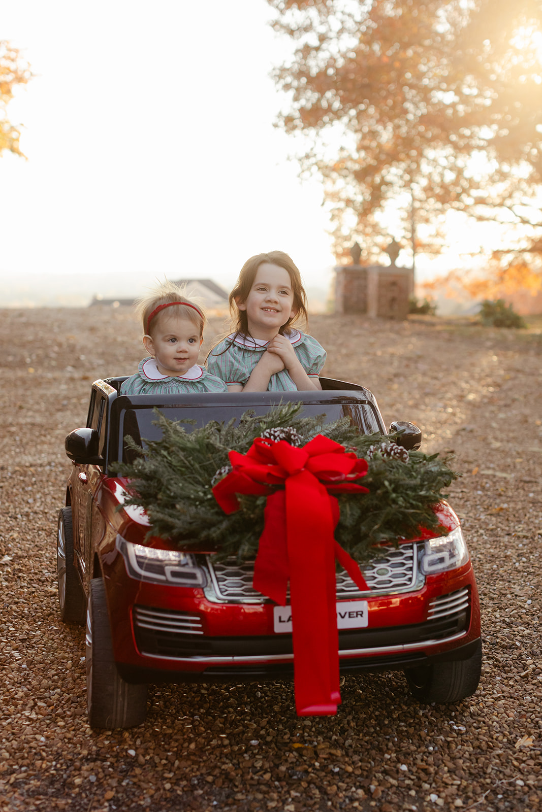 little sisters in red toy car. christmas family photos in front of home