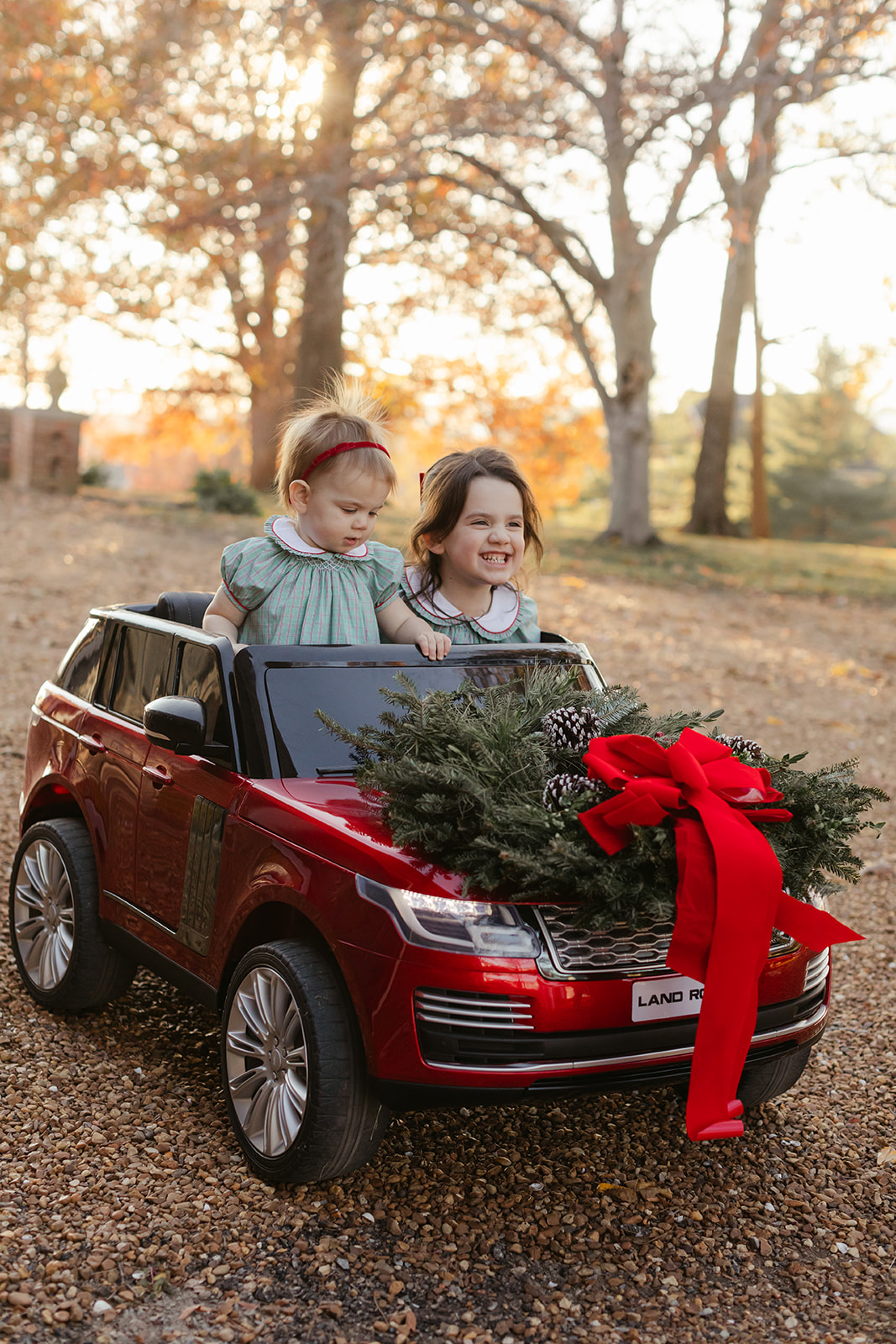 little sisters in red toy car. christmas family photos in front of home