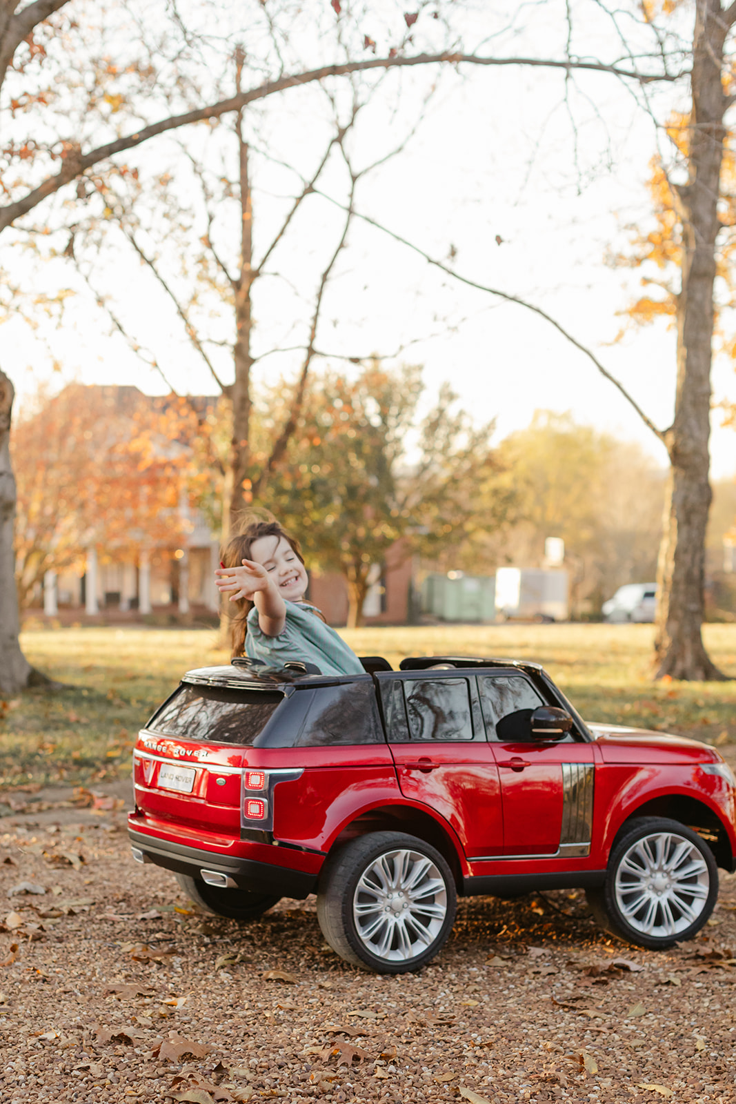 little girl waving riding her red toy car. christmas family photos in front of home