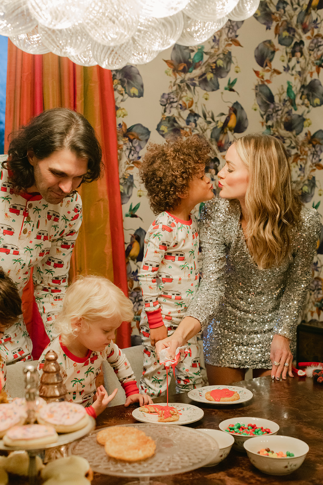 kids in Christmas pj's, dad in matching pj's and mom in sparkly sequen dress decorating cookies. Christmas family photos in home