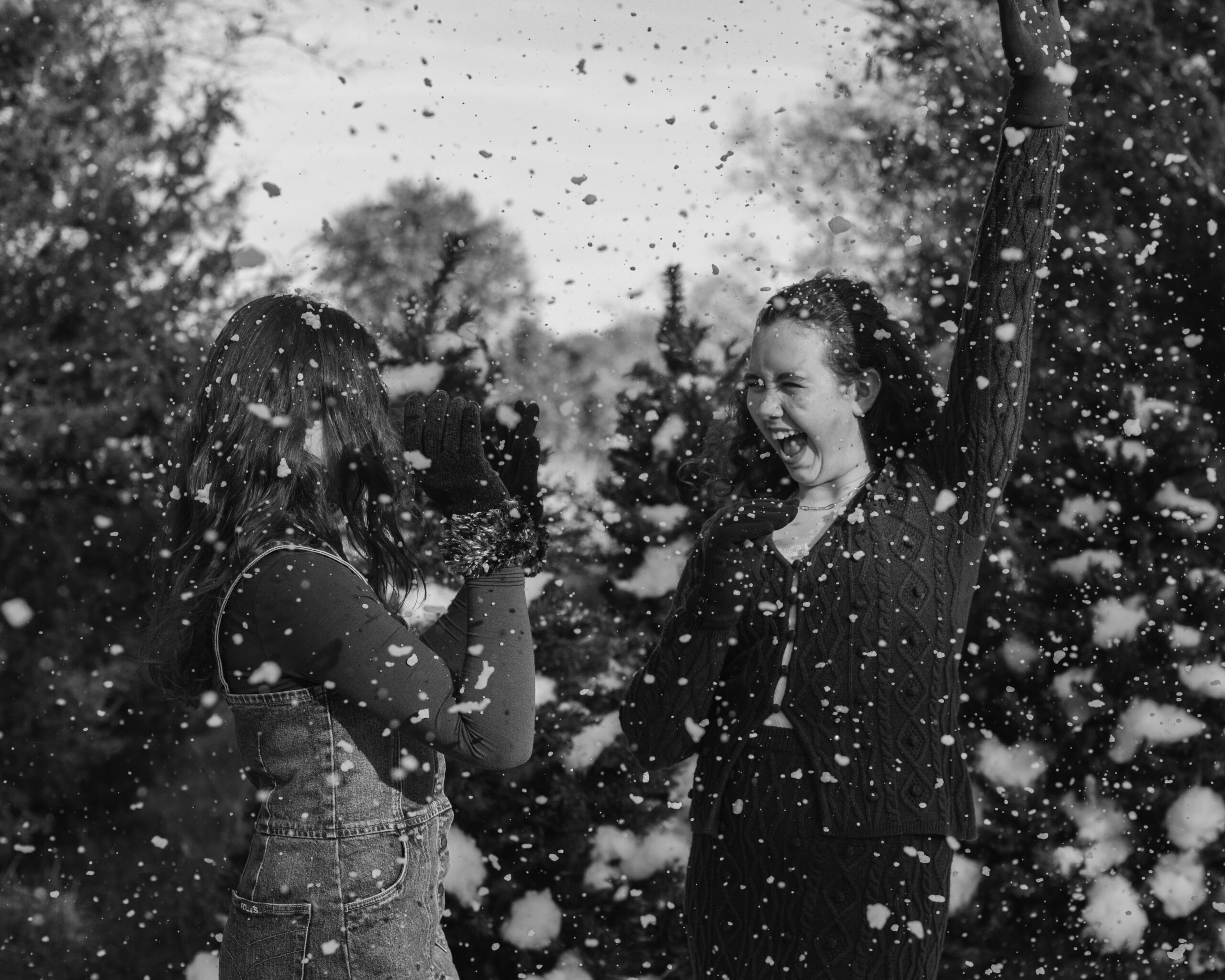 two sisters in cute brown winter outfits wearing beanies laying on the ground surrounded by fake snow for winter christmas photos