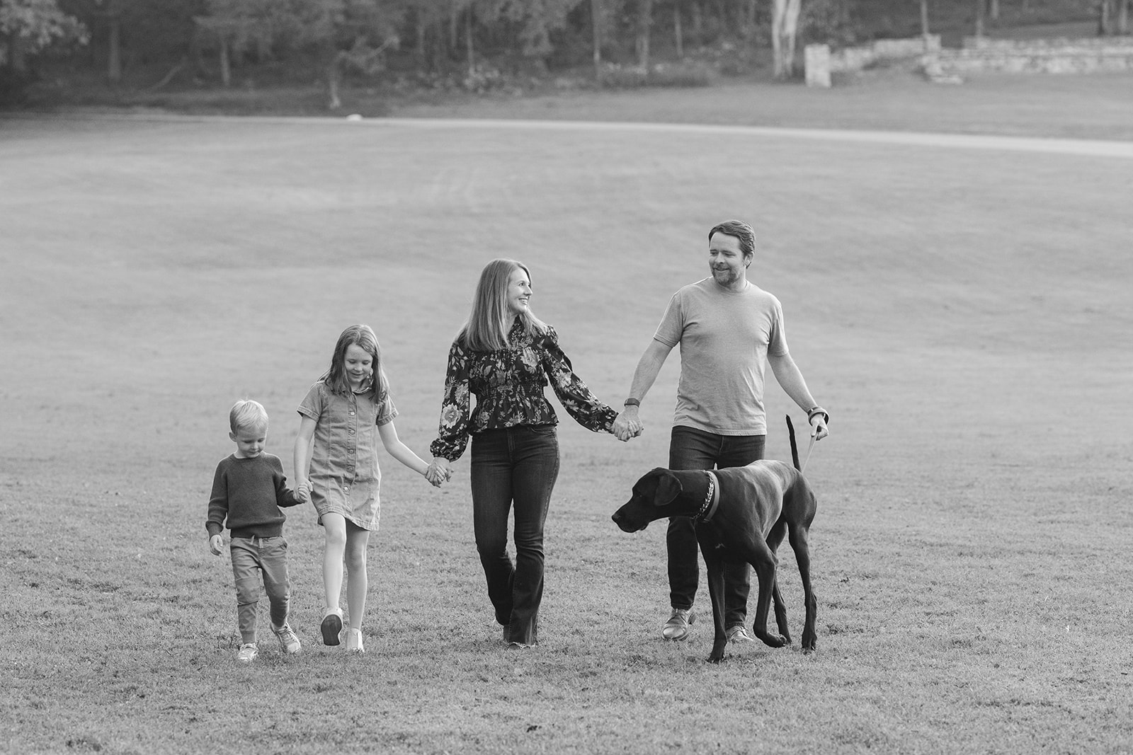 a family of four and their dog walk together laughing and playin during family photos.