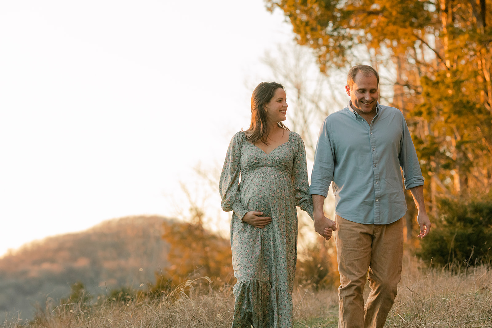 a pregnant woman walks while holding her partner's hand during their sunset maternity photos in Nashville, Tn. 