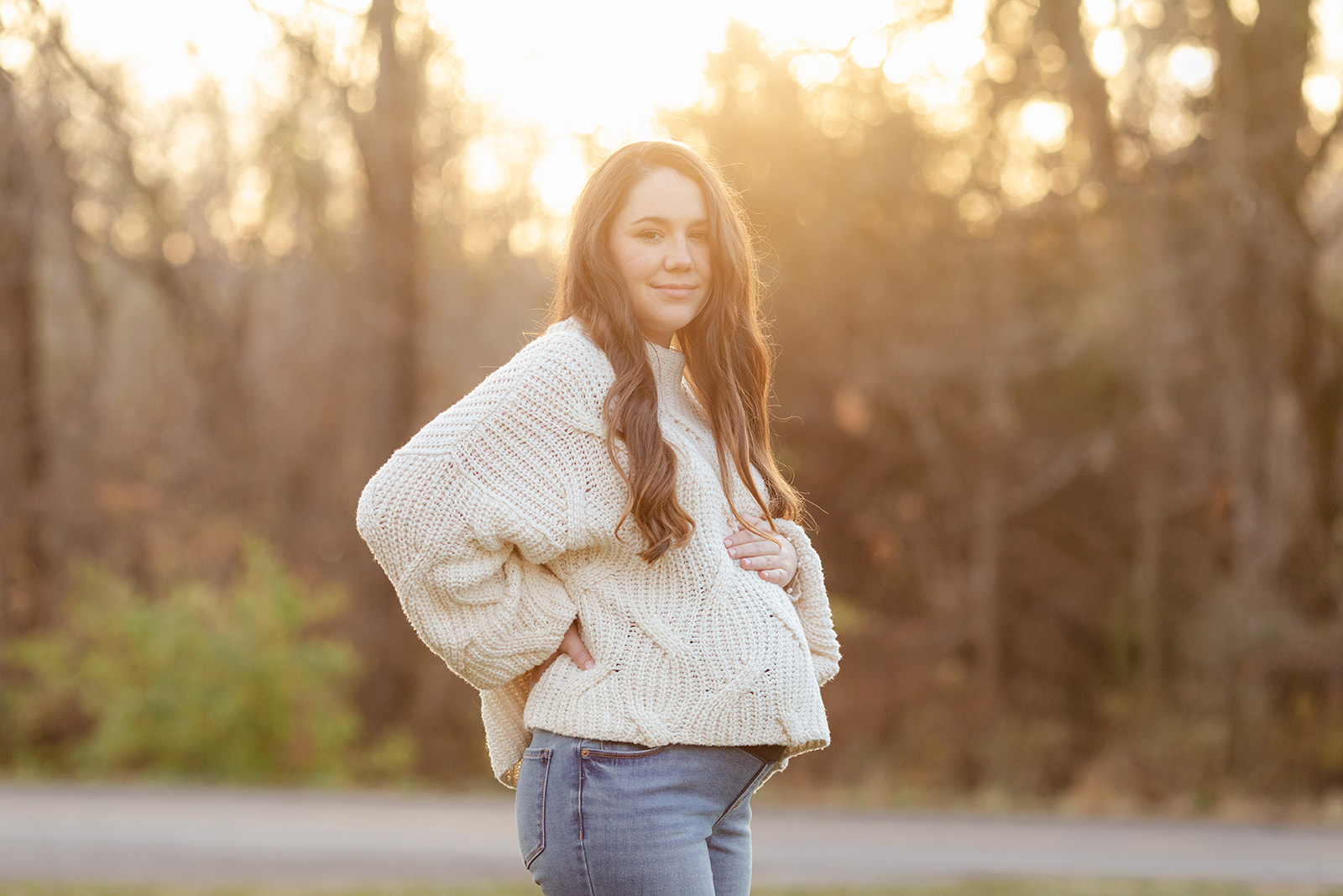 An expectant mother poses for maternity photos in golden hour light of sunset.