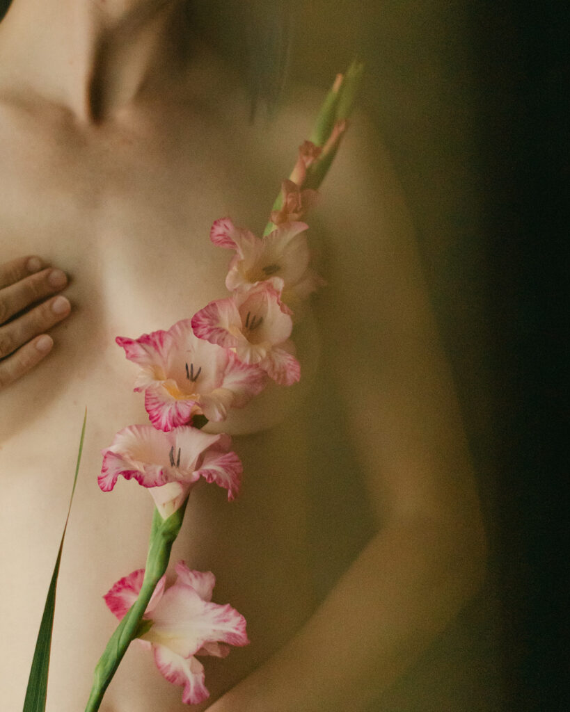 a woman holds a gladiola flower over her breast