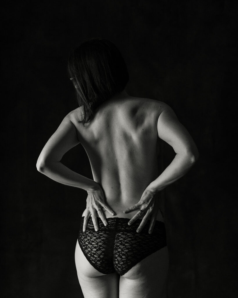 Nashville Boudoir Photographer photographs the back of a woman standing against a black backdrop