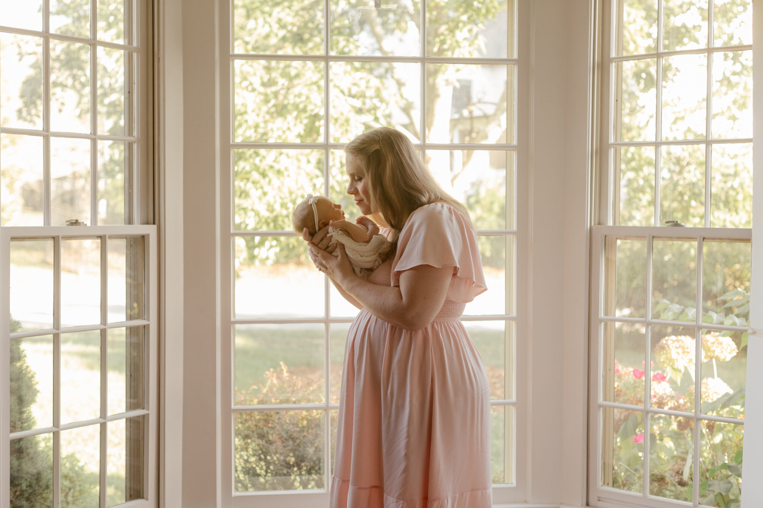 mama with newborn daughter standing by window.