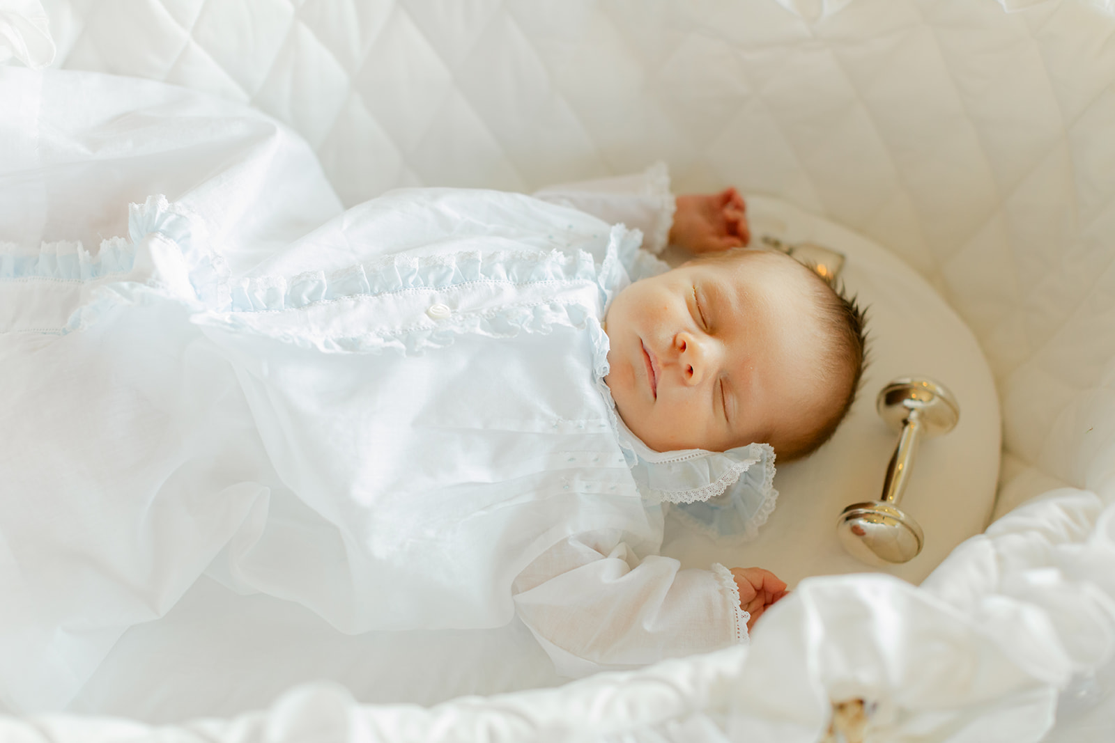 newborn baby boy in white outfit in bassinet