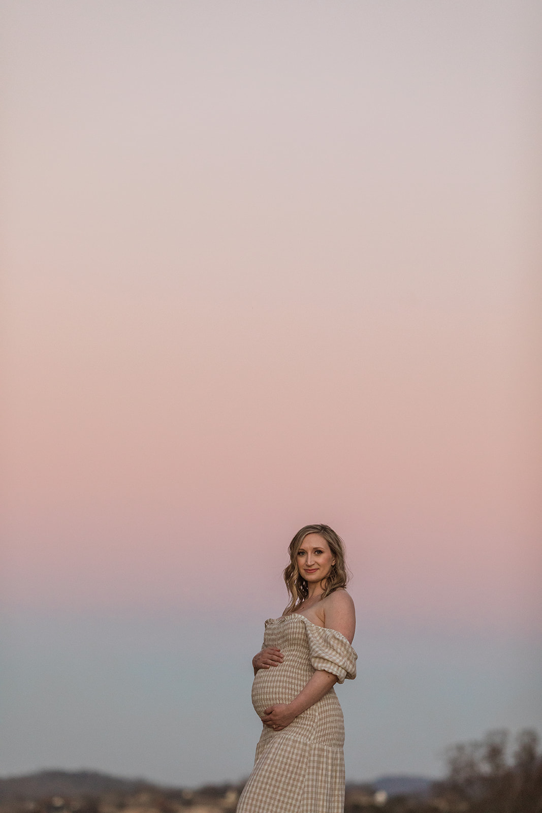 expecting mama posing during sunset maternity session, pink skies