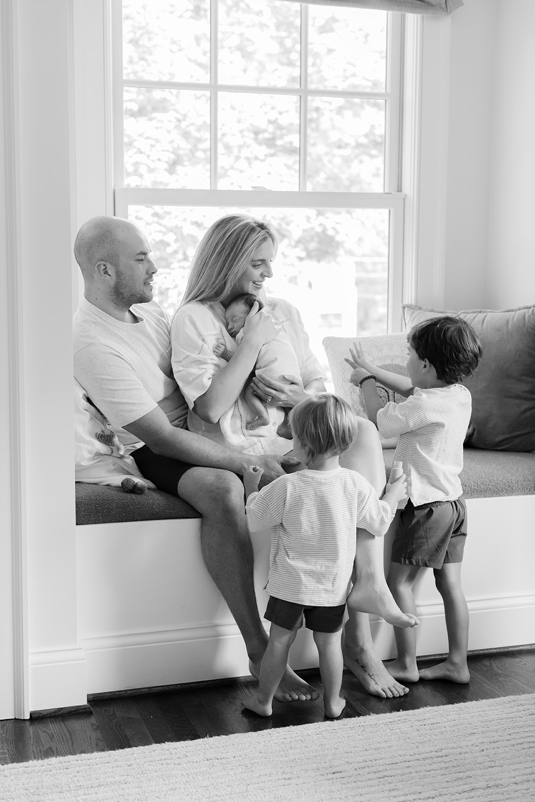 family of 5 sitting on windowsill, dad reading children's book
