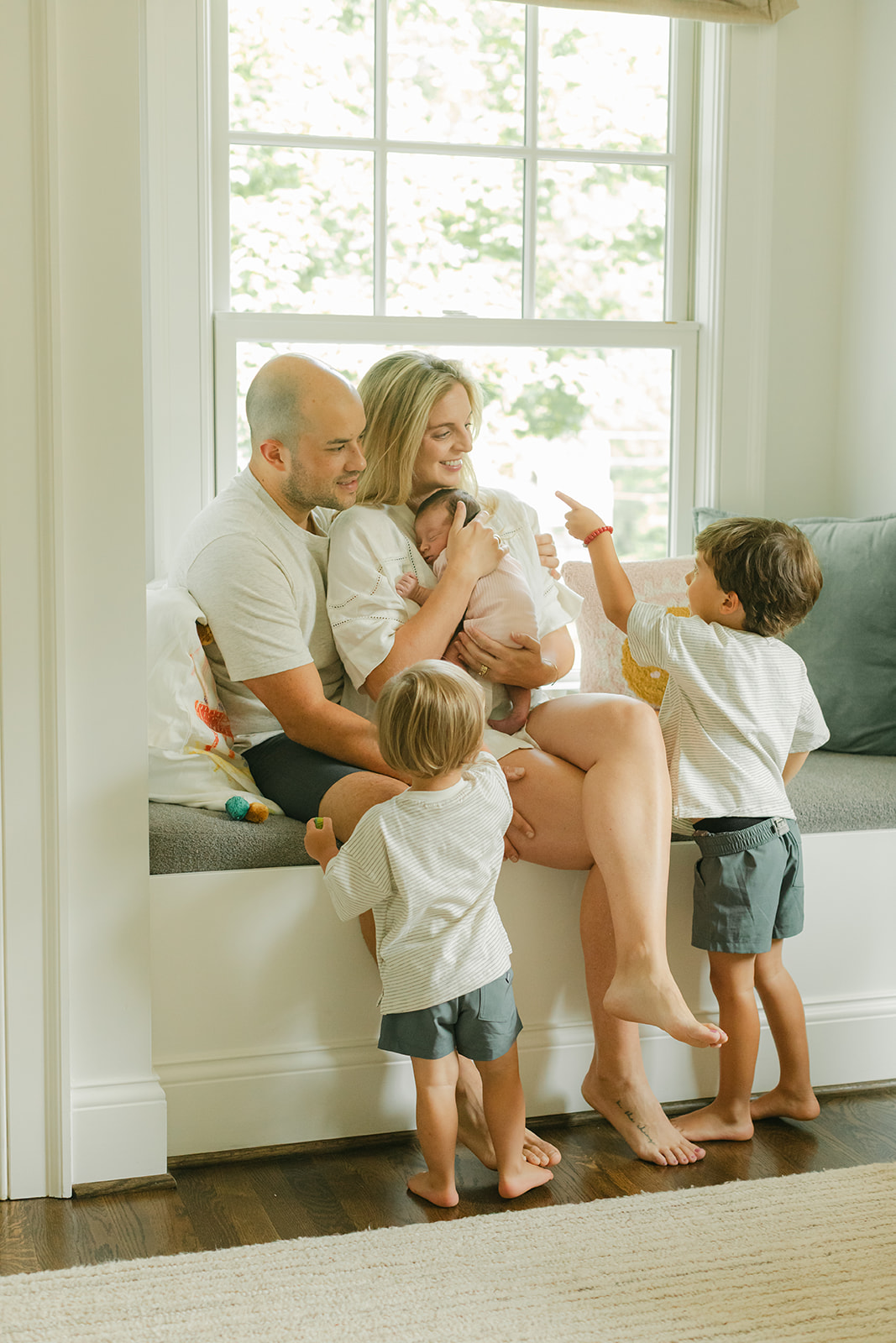 family of 5 sitting on windowsill, dad reading children's book