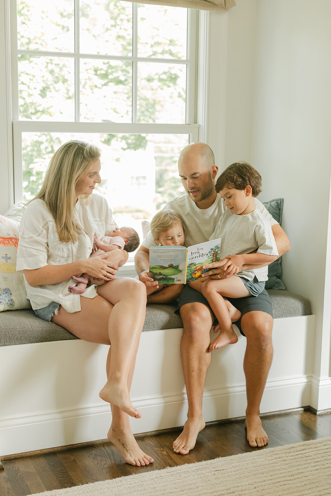 family of 5 sitting on windowsill, dad reading children's book